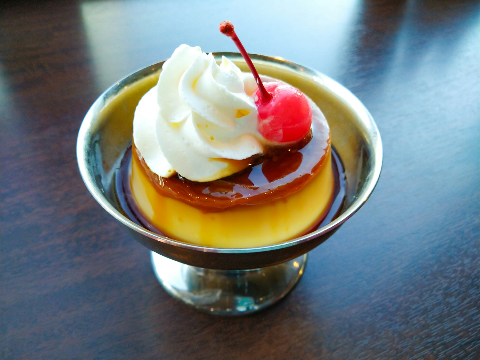 Vanillepudding-Dessert mit Sahne und einer Kirsche garniert