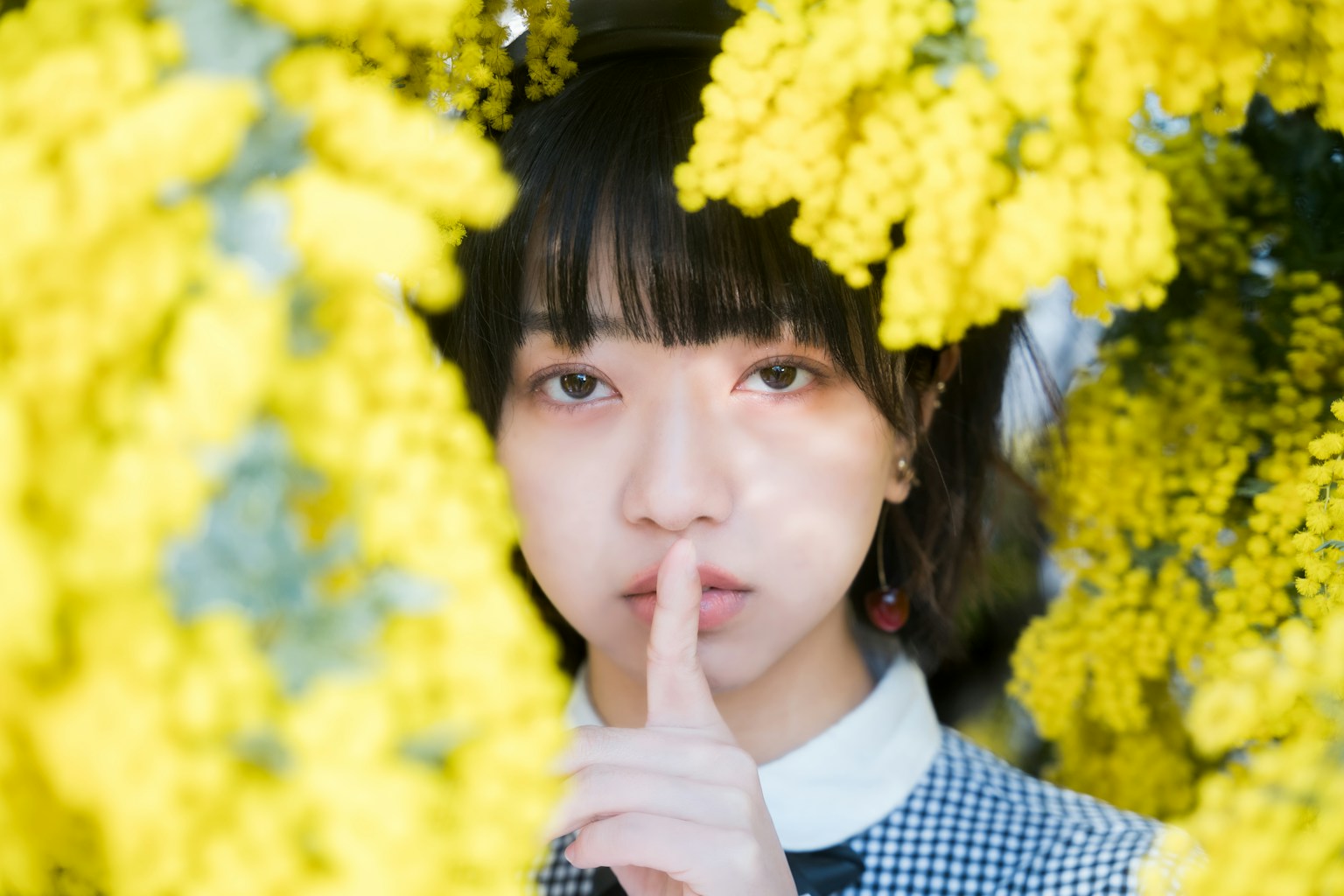 Close-up of a woman surrounded by yellow flowers making a shushing gesture