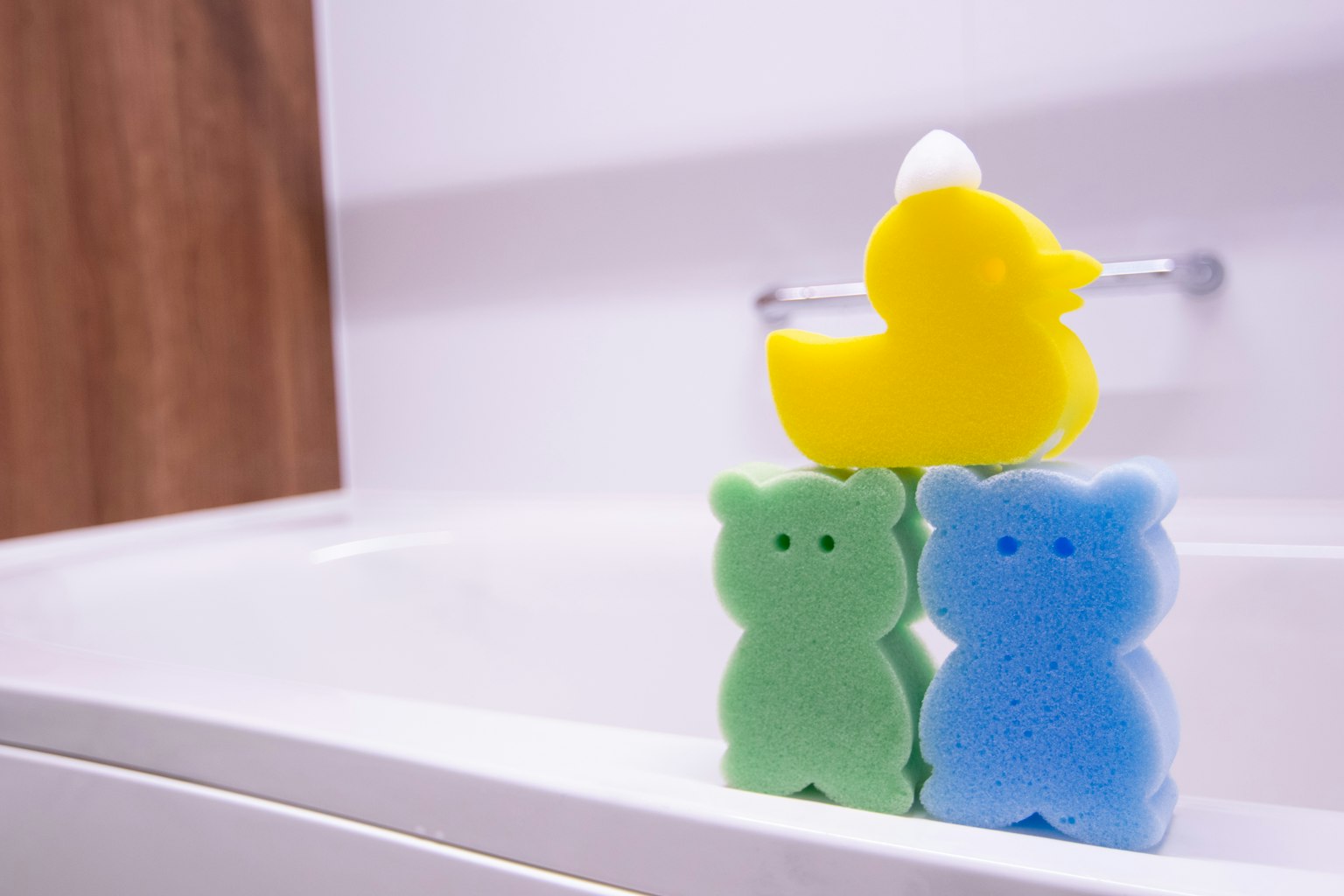 Ours en éponge colorés empilés à côté d'un canard en caoutchouc jaune au bord d'une baignoire