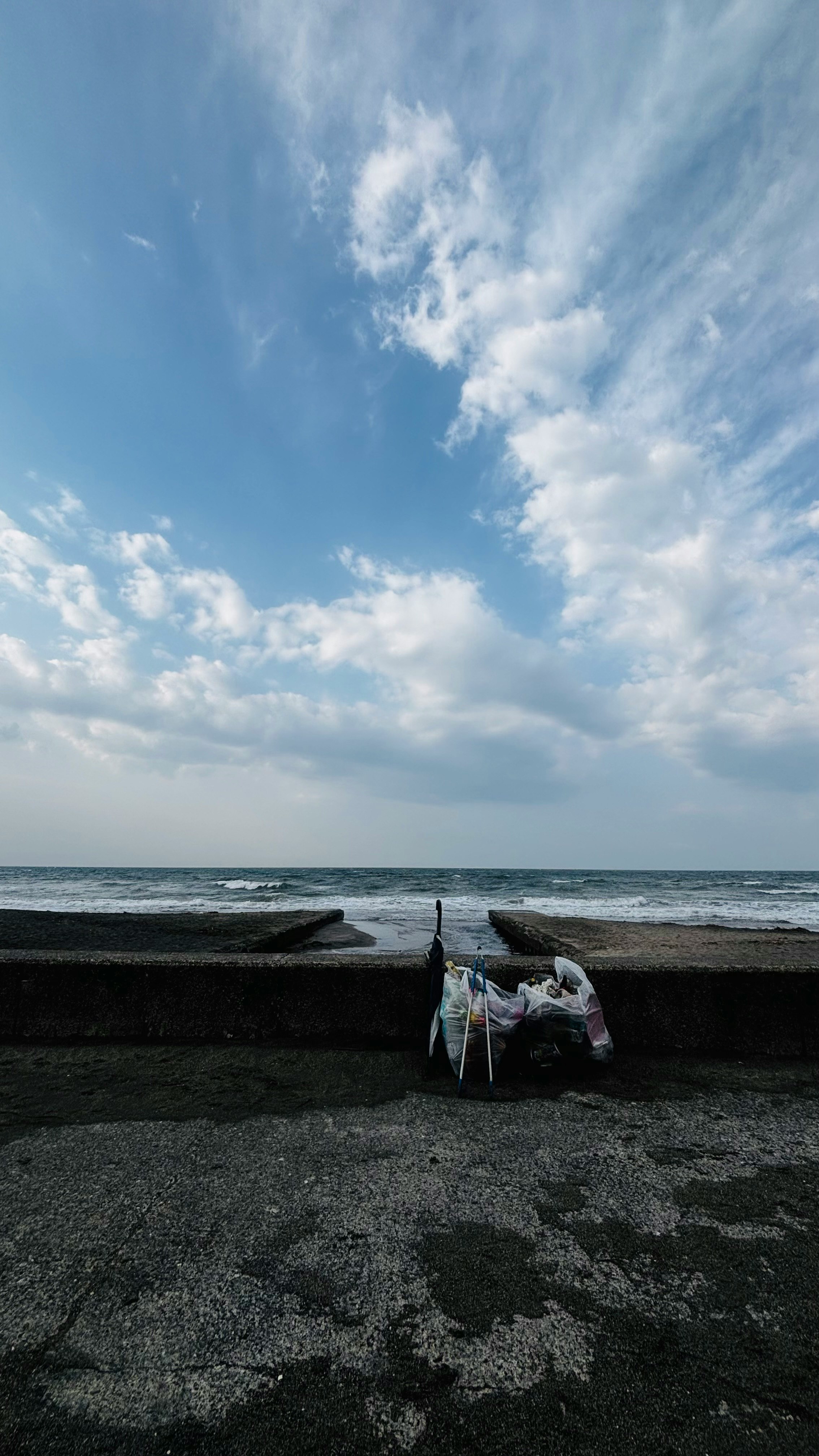 海辺の防波堤とゴミ袋を拾う人のある砂利の浜