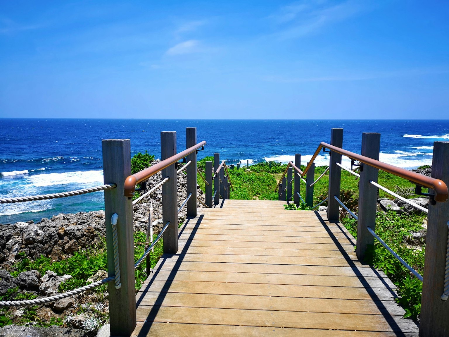 Wooden pathway leading to the blue ocean under a clear sky