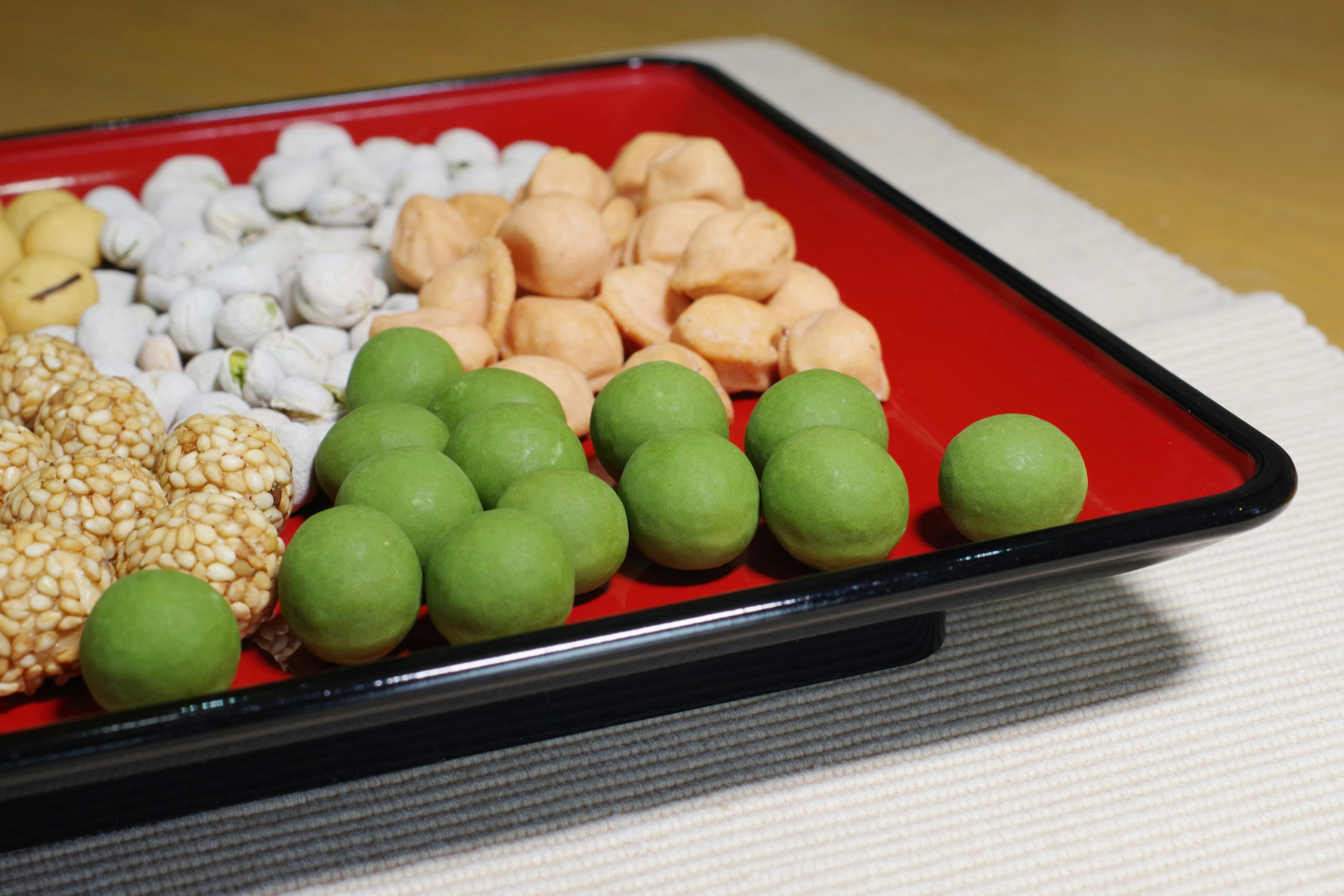Colorful Japanese sweets arranged on a red plate featuring green dumplings and white snacks