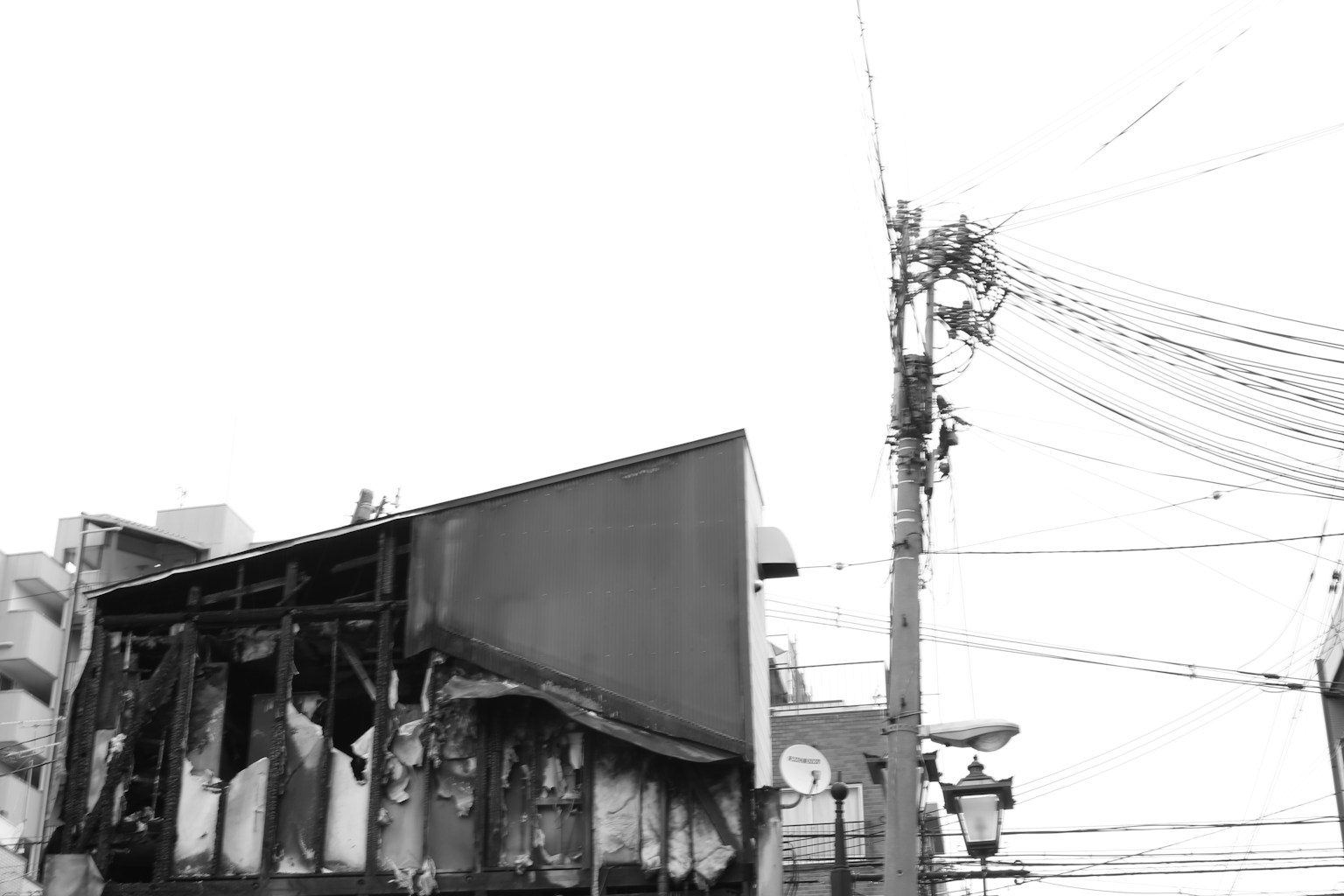 Imagen en blanco y negro de una valla publicitaria quemada y un poste de electricidad