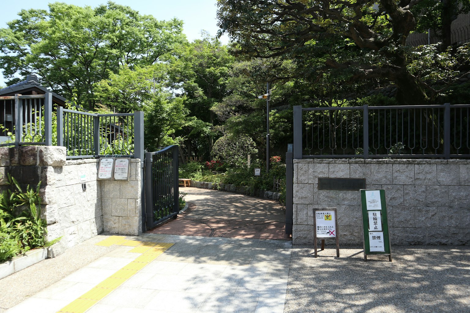 郁郁蔥蔥的公園入口，石牆和鐵圍籬，入口處有一個標牌