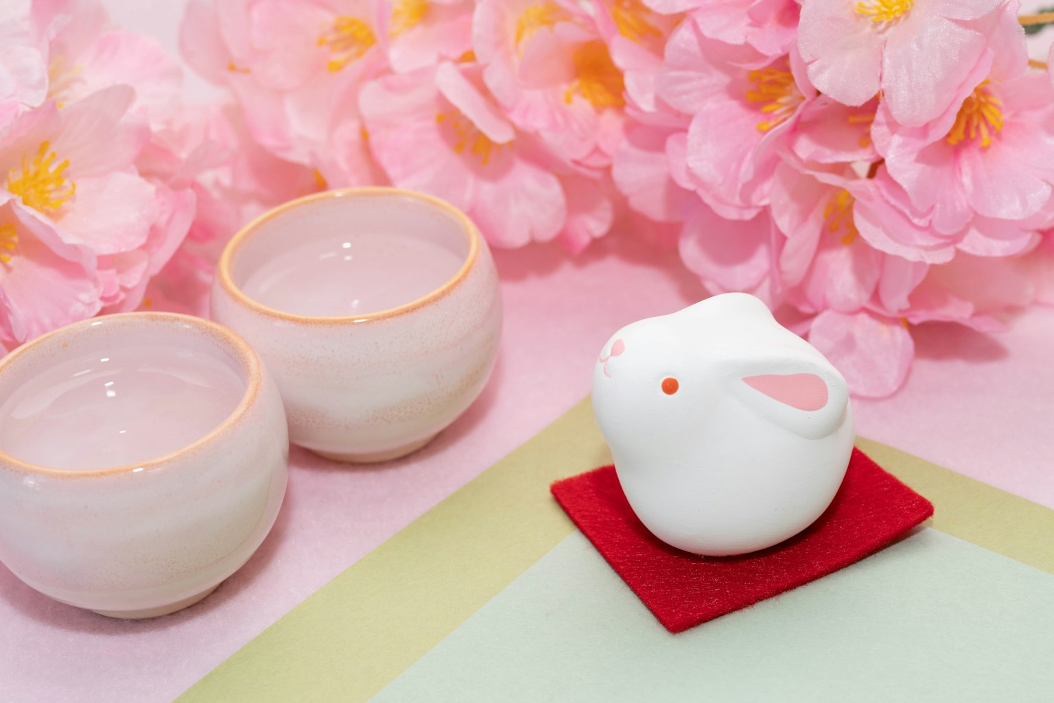Tượng thỏ gốm trắng đặt giữa hoa hồng cùng hai bát nhỏ