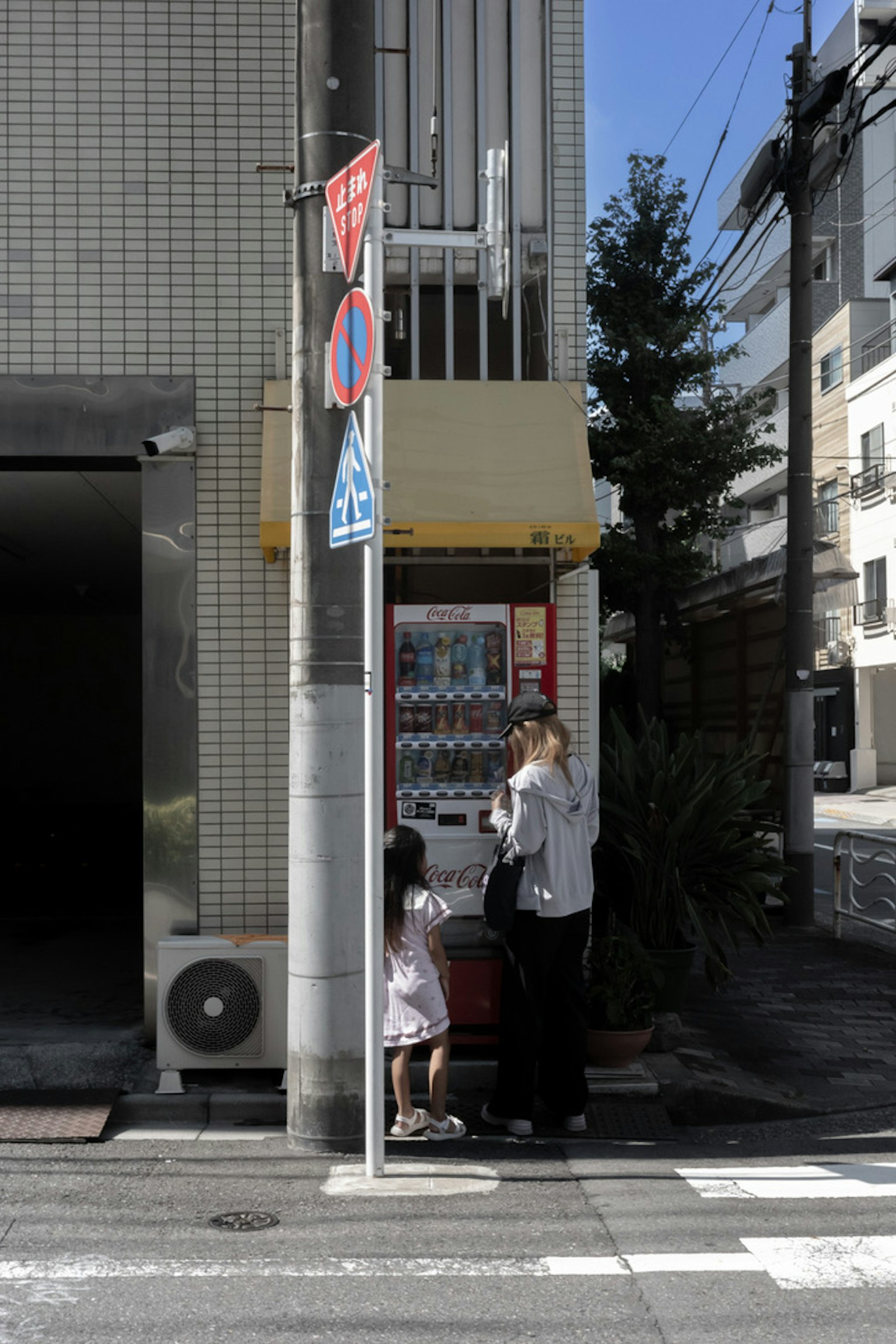 Silhouette di un genitore e un bambino davanti a un distributore automatico all'angolo di una strada con edifici circostanti