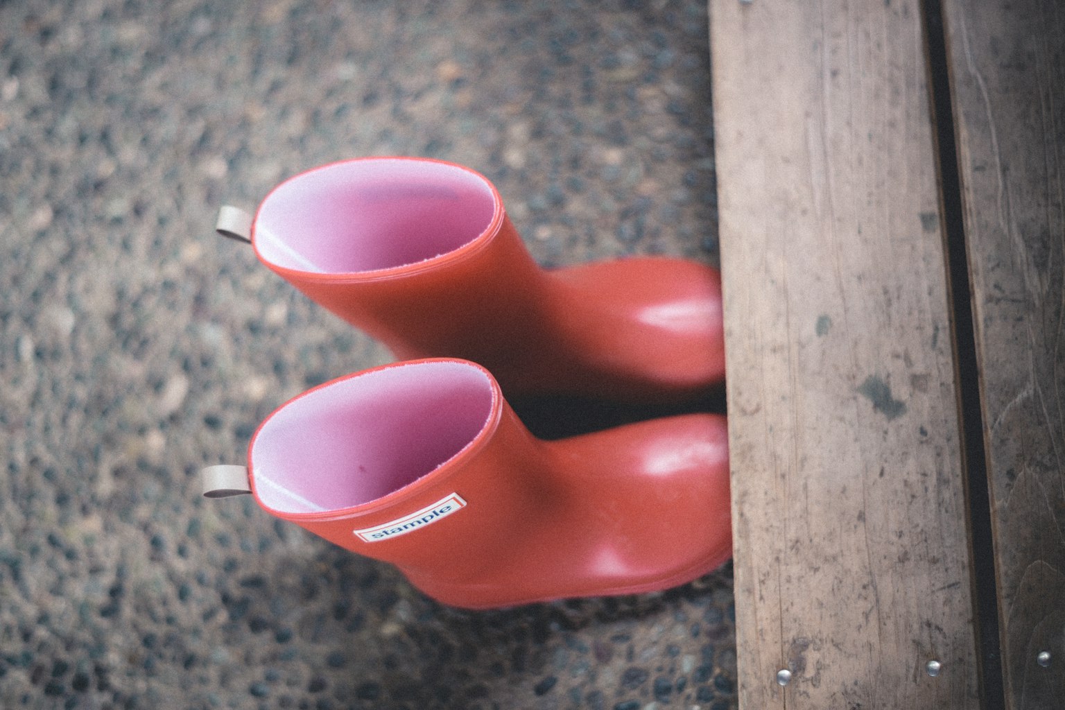 Botas de goma rojas colocadas cerca de una tabla de madera