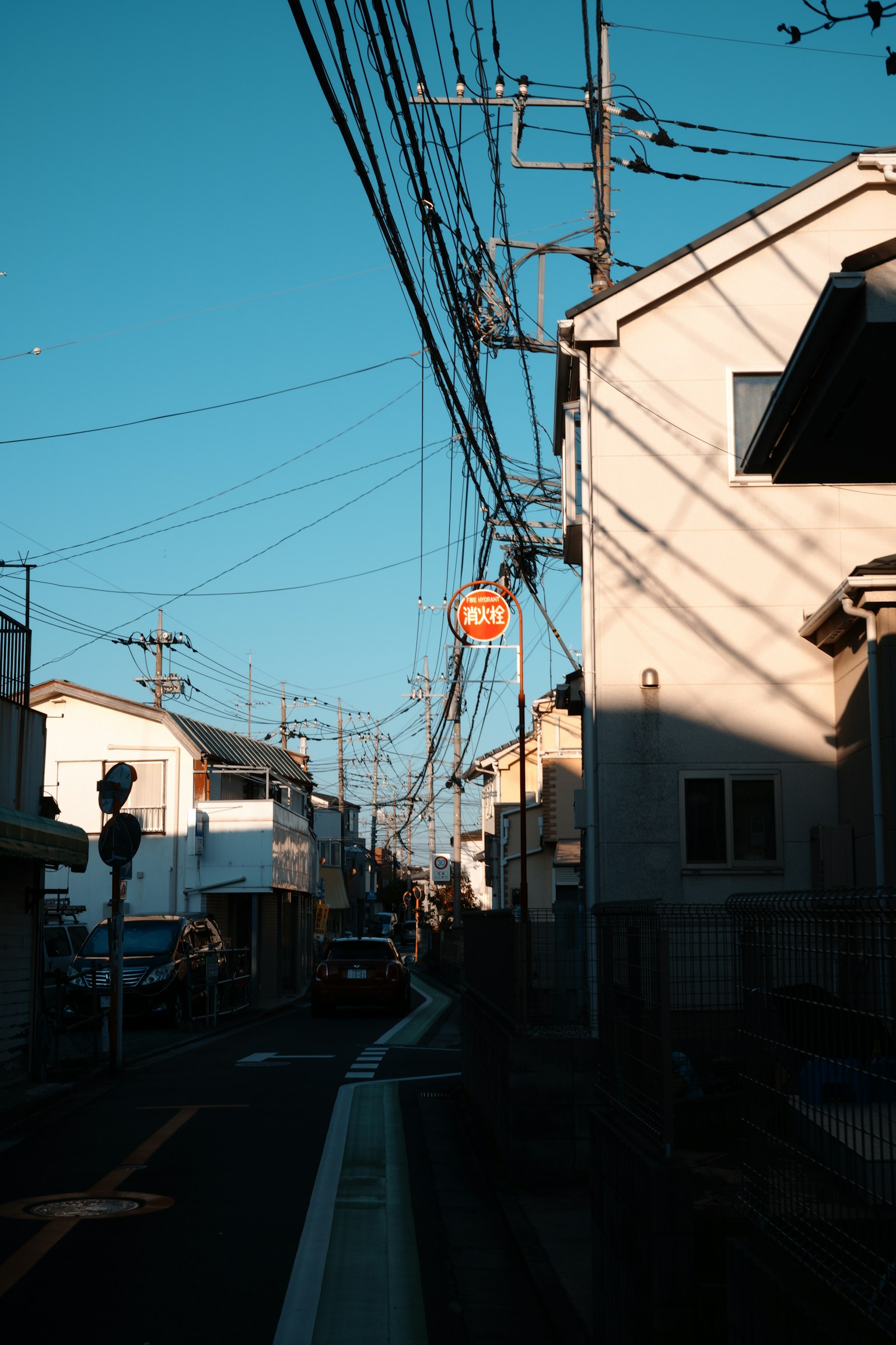 Street view of a residential area with power lines and shadows under a blue sky