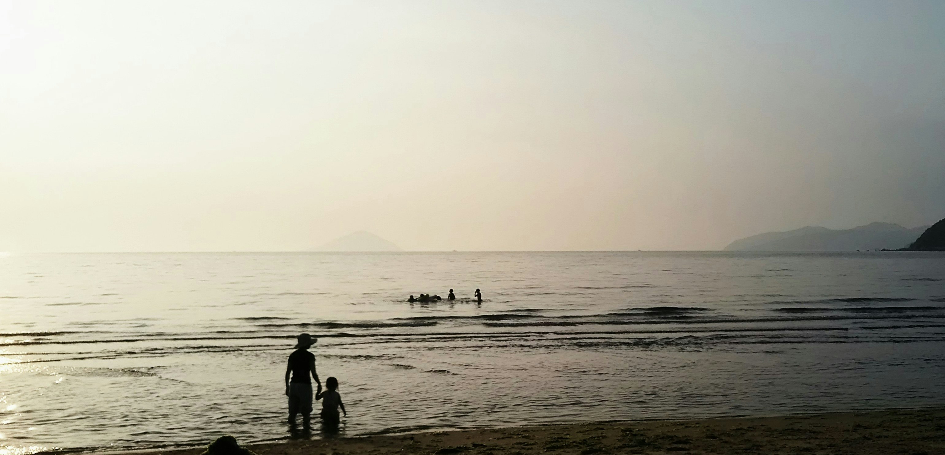 persone sulla spiaggia al tramonto, onde calme e orizzonte