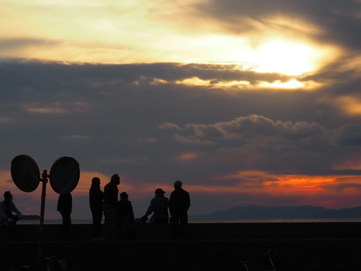 Silhouetten von Menschen gegen einen Sonnenuntergang mit Wolken