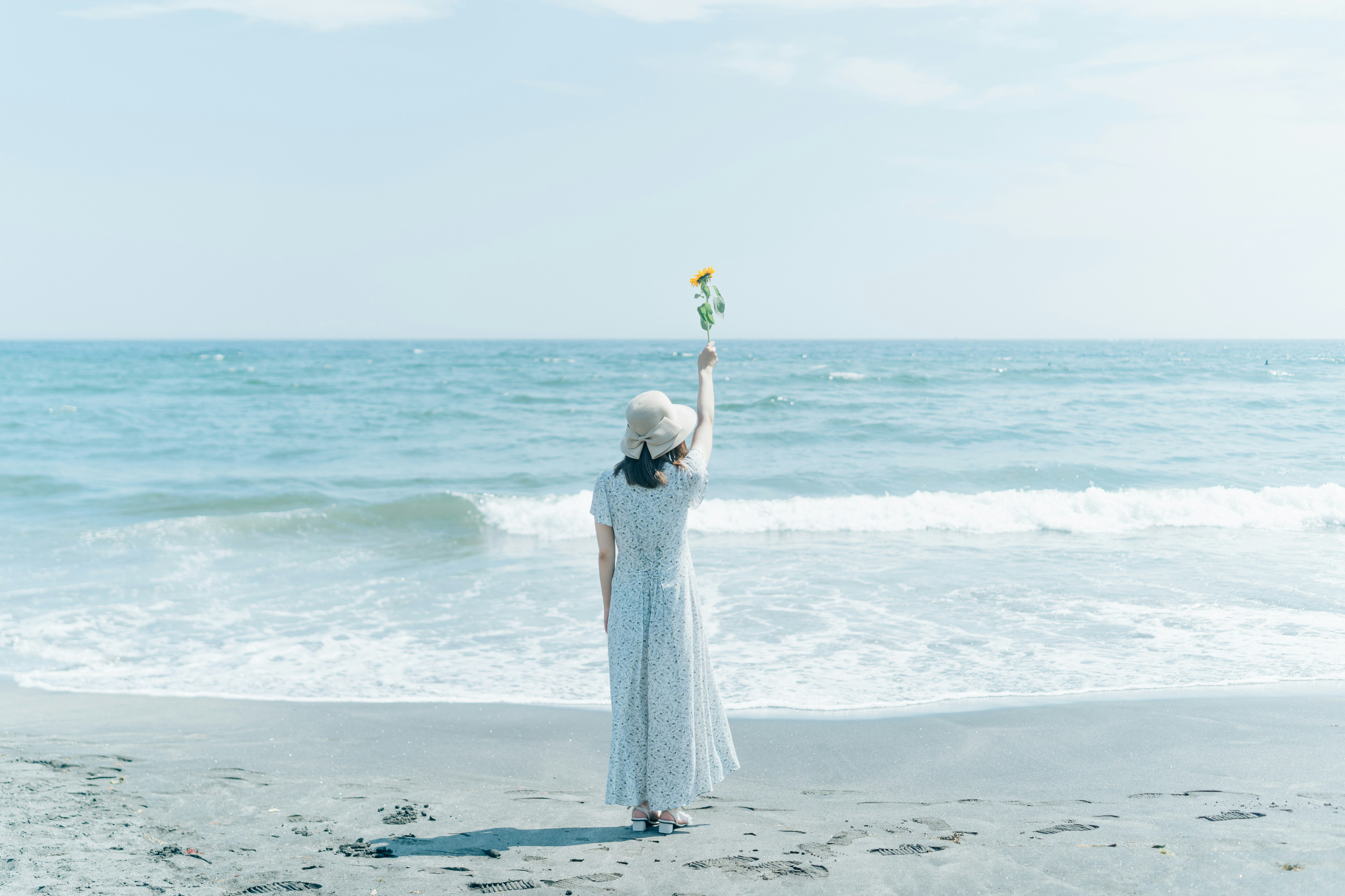 夏の海辺で手を上げる白いドレスの女性の後ろ姿