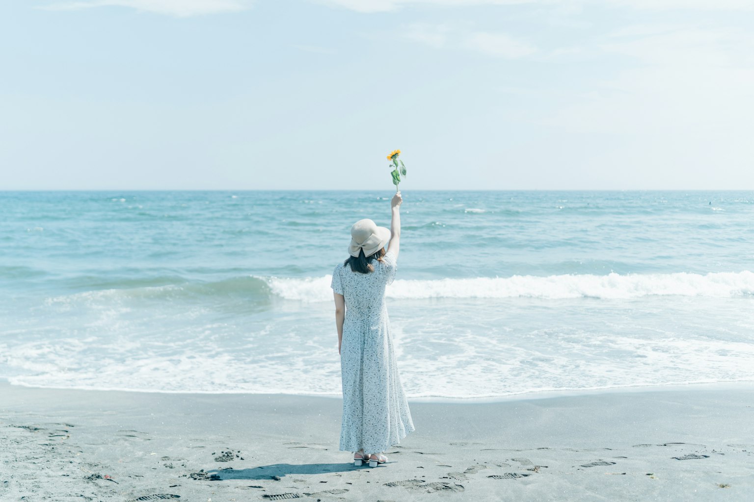 Mujer con vestido blanco sosteniendo una flor en la playa