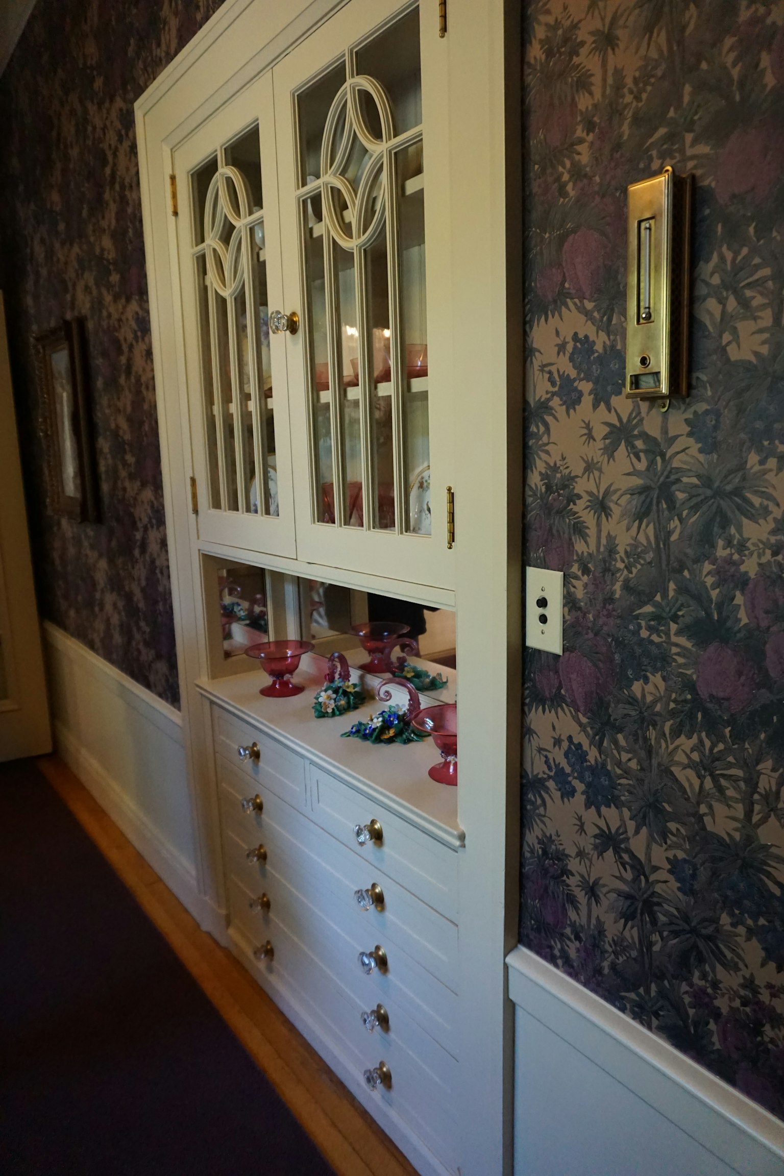 Ein Flur mit einem weißen Schrank mit Glastüren und floralem Tapeten