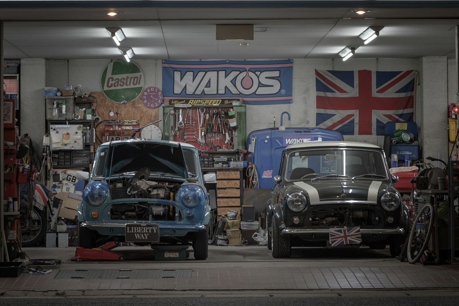 Interior of a garage with a blue Mini and a black Mini tools and a WAKOS banner visible