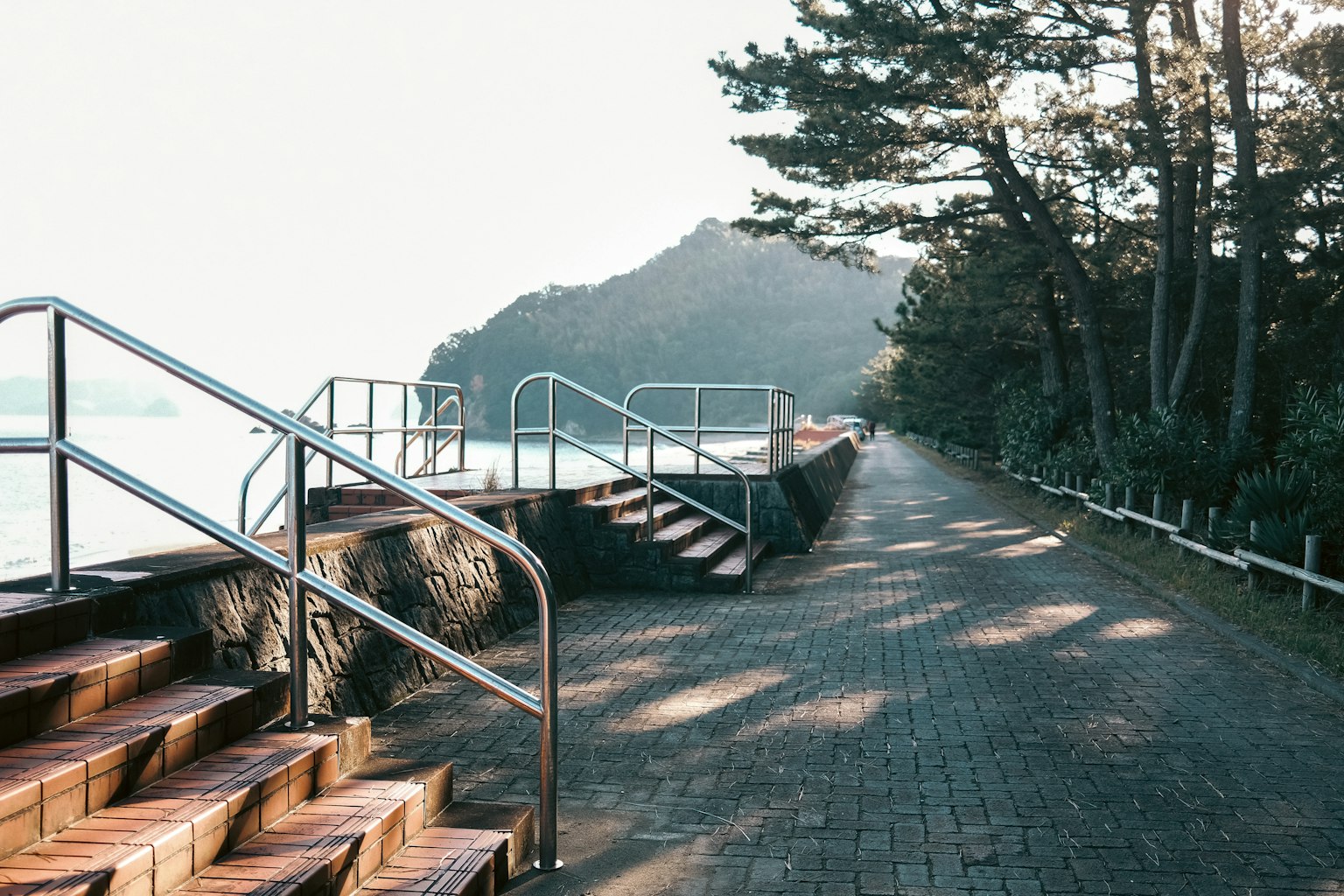 Terrazza in legno e scale lungo la costa con alberi verdi e montagne sullo sfondo