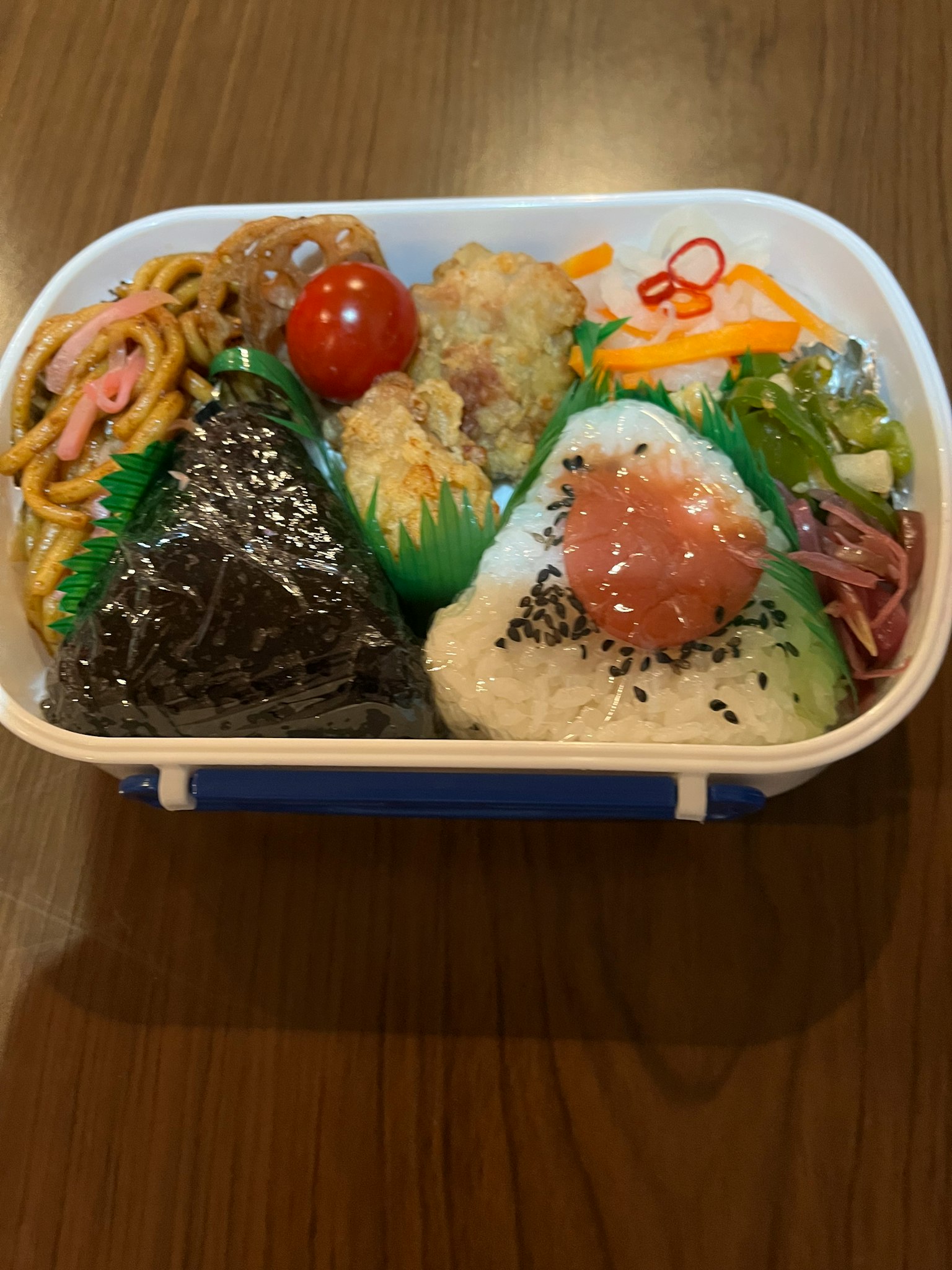 Colorful bento box with various foods Rice balls wrapped in seaweed Fried chicken Cherry tomato Vegetable salad