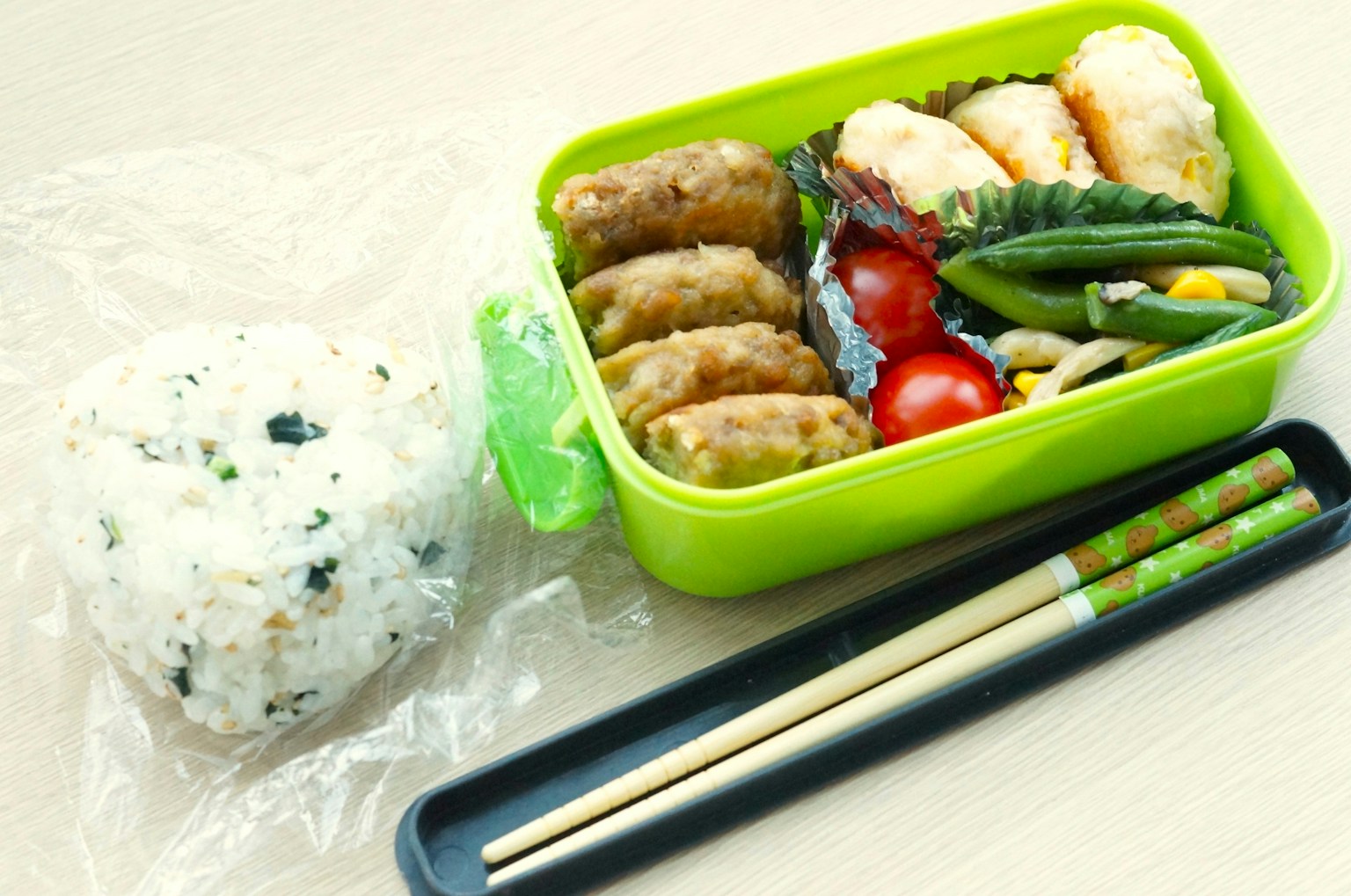 緑の弁当箱に詰められたおかずと小さなご飯の塊