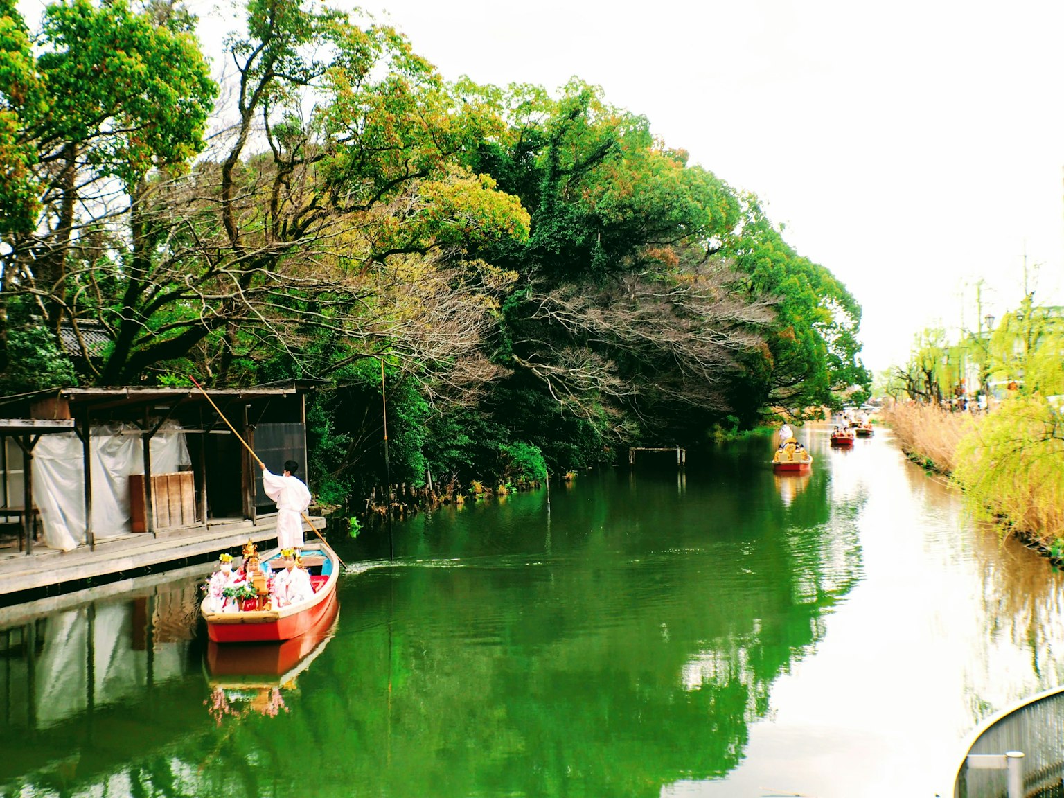 Một chiếc thuyền nhỏ màu đỏ đang di chuyển trên một con kênh xanh bao quanh bởi cây cối tươi tốt