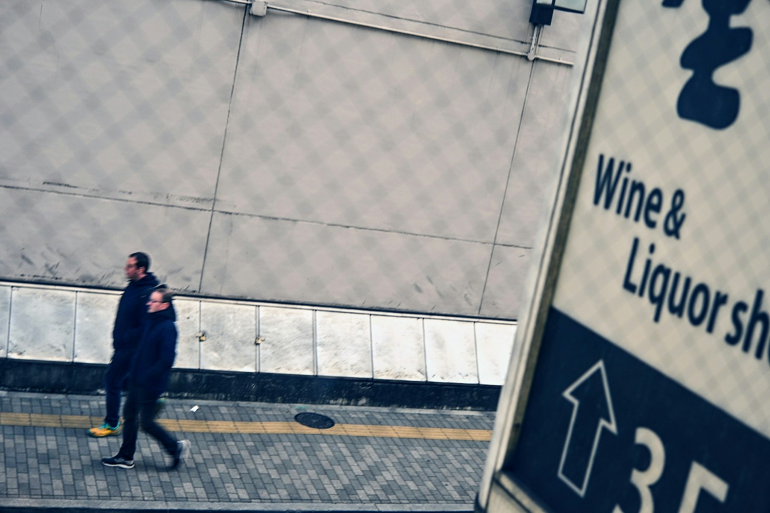 Due uomini che camminano davanti a un'insegna di vino e liquori