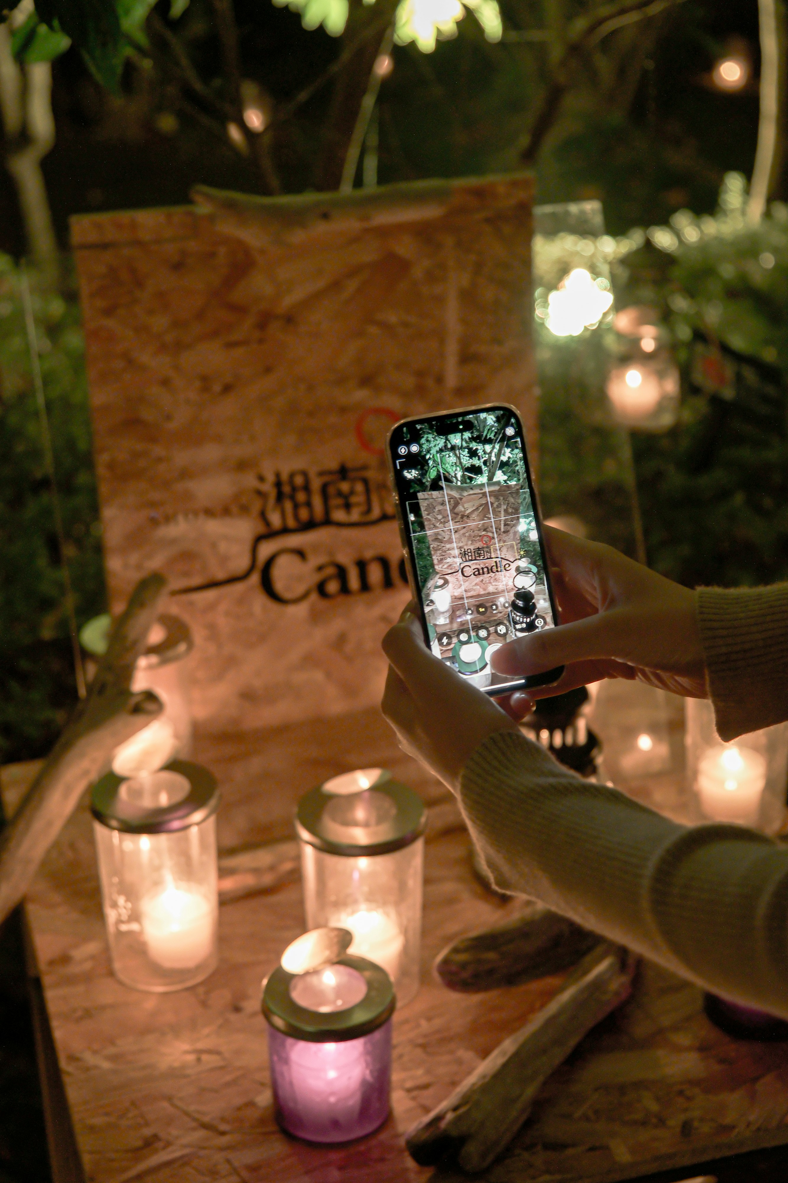 キャンドルの灯る屋外のテーブルでスマホを撮影する手