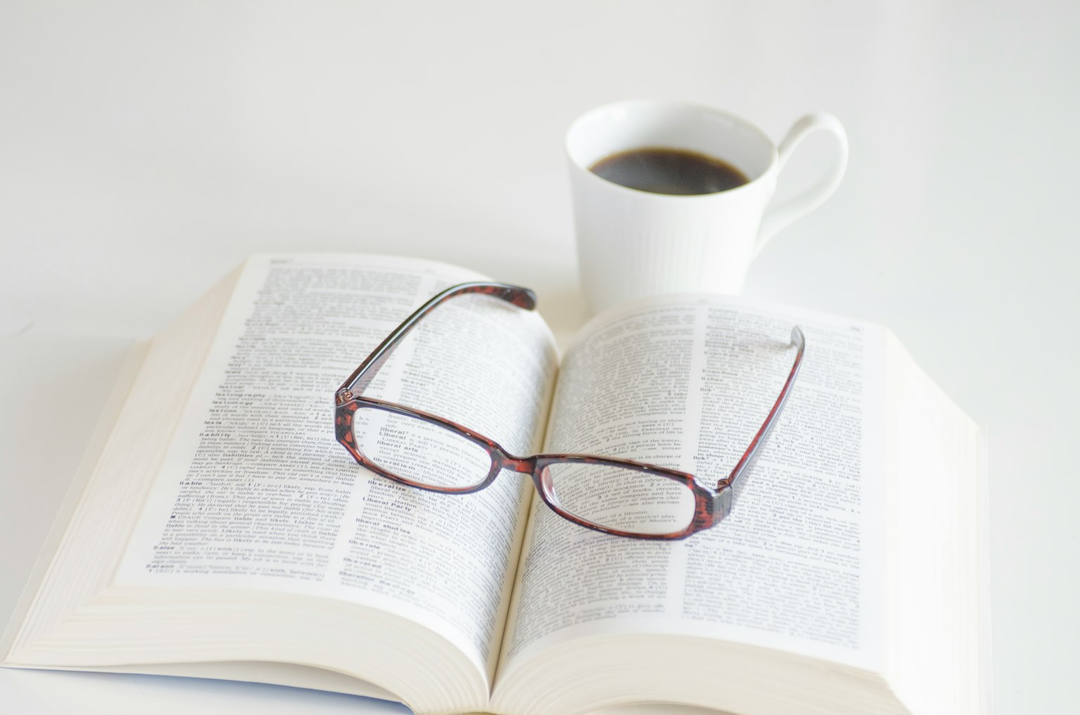 Gafas descansando sobre un libro abierto junto a una taza de café