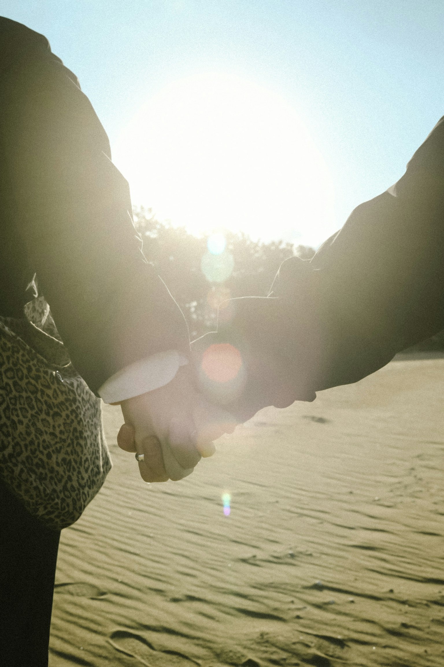 Silhouette d'un couple se tenant par la main sous le soleil sur une plage de sable