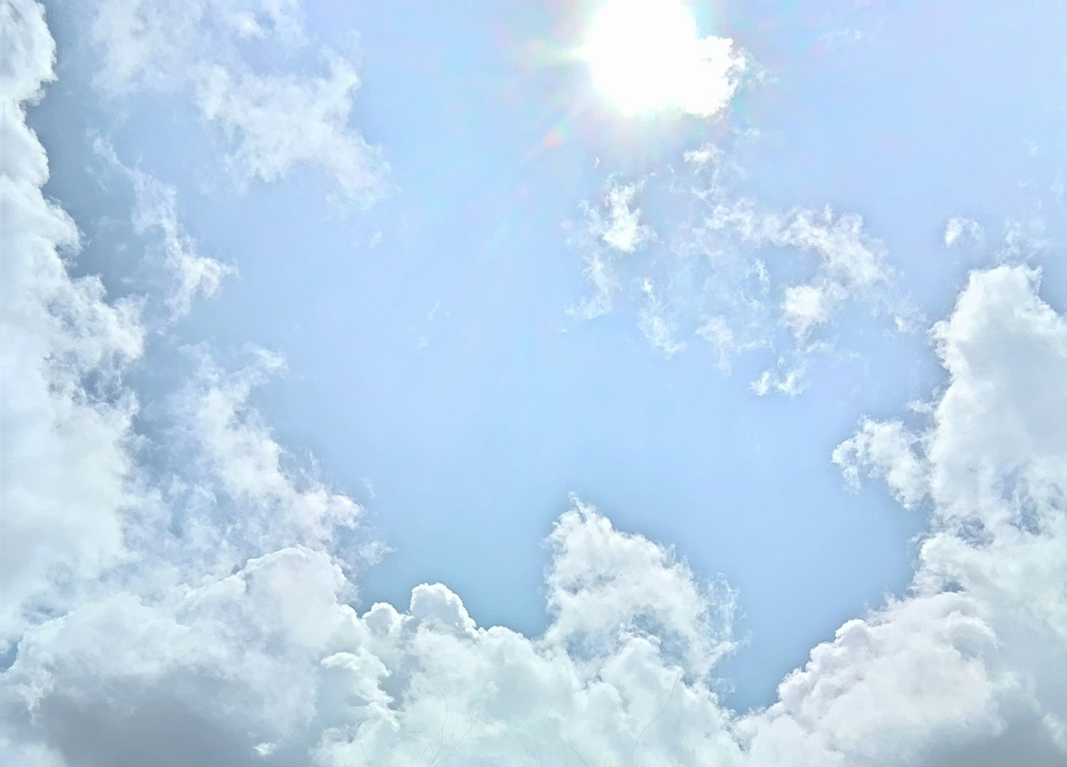 Bright blue sky with fluffy white clouds and shining sun