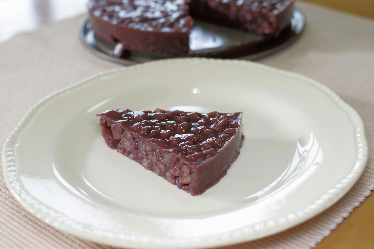 Irisan kue kacang merah di piring putih dengan kue lainnya di latar belakang