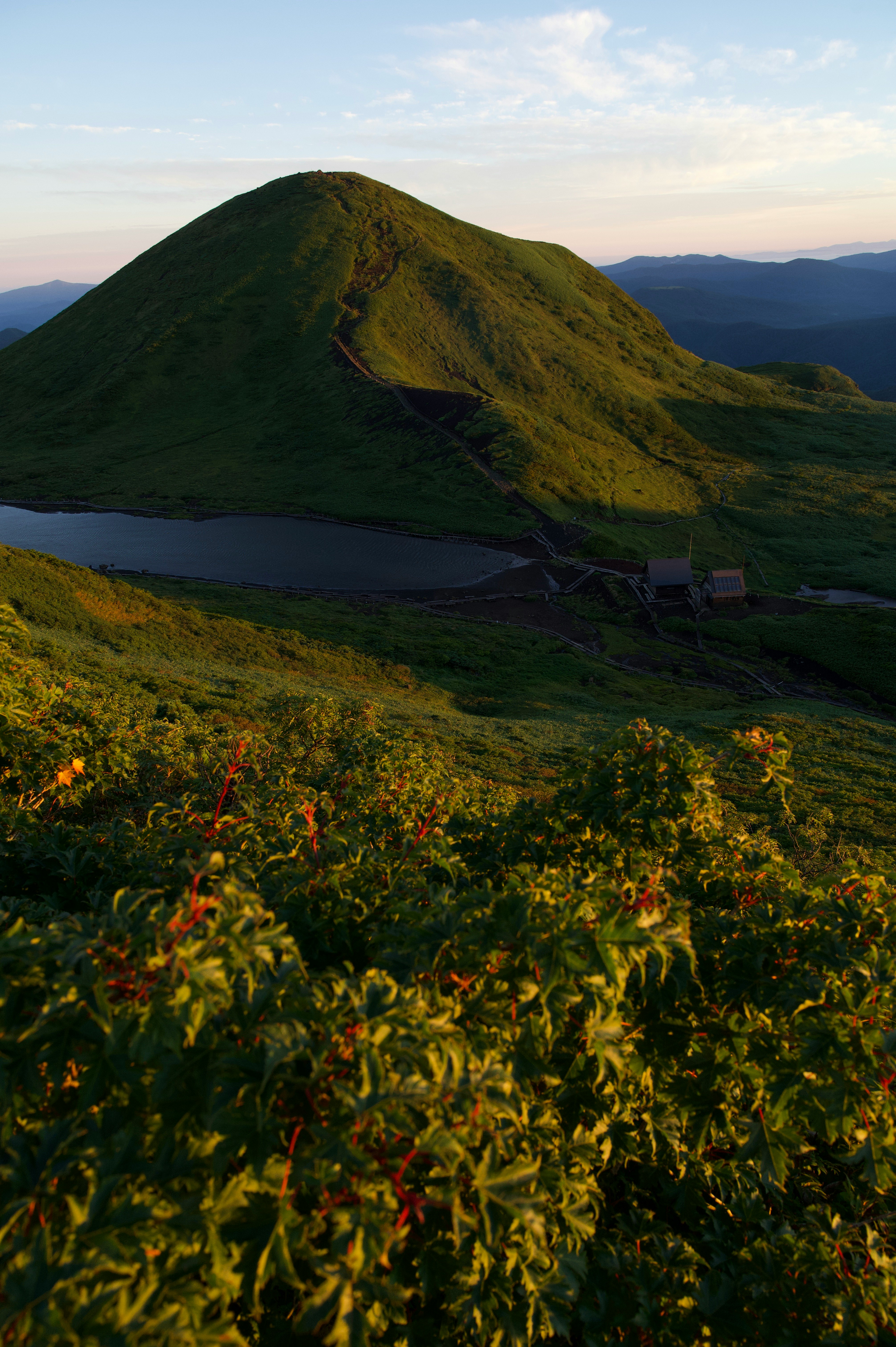 vista de una cresta montañosa y un lago desde una ladera herbosa al atardecer