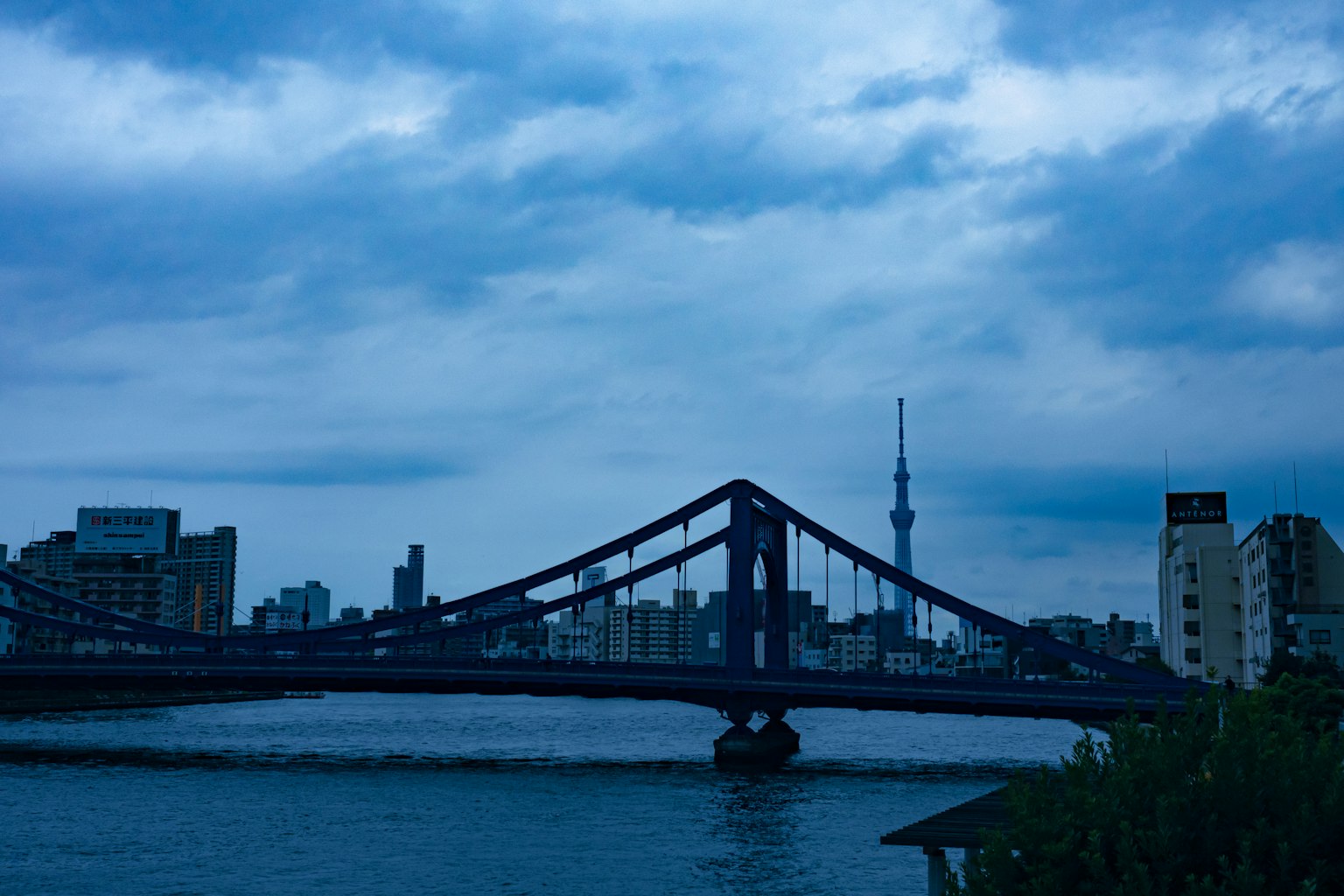 Blick auf eine Brücke mit Tokyo Skytree im Hintergrund unter dunklen Wolken