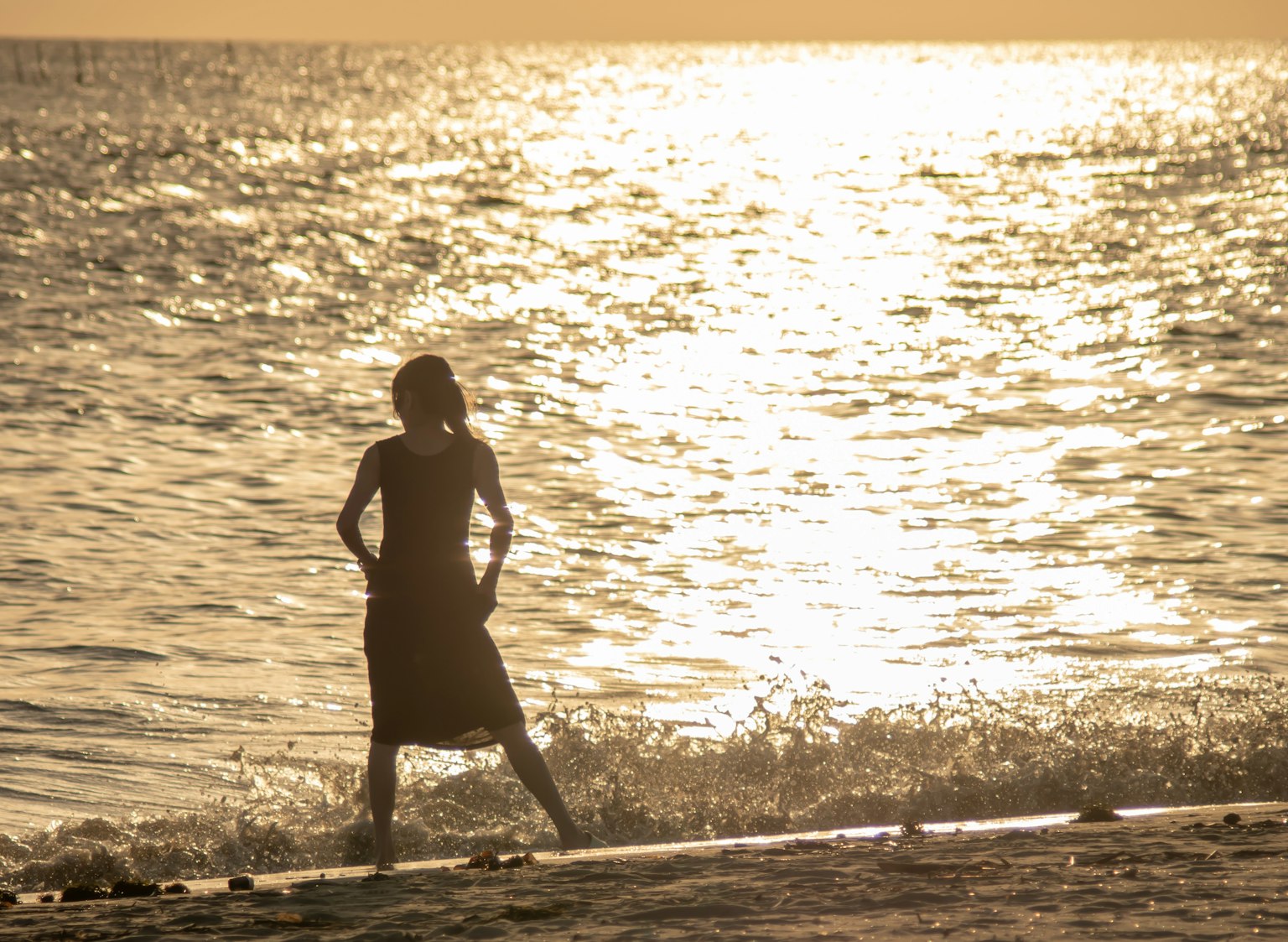 夕日を背景に海辺で立つ女性のシルエット
