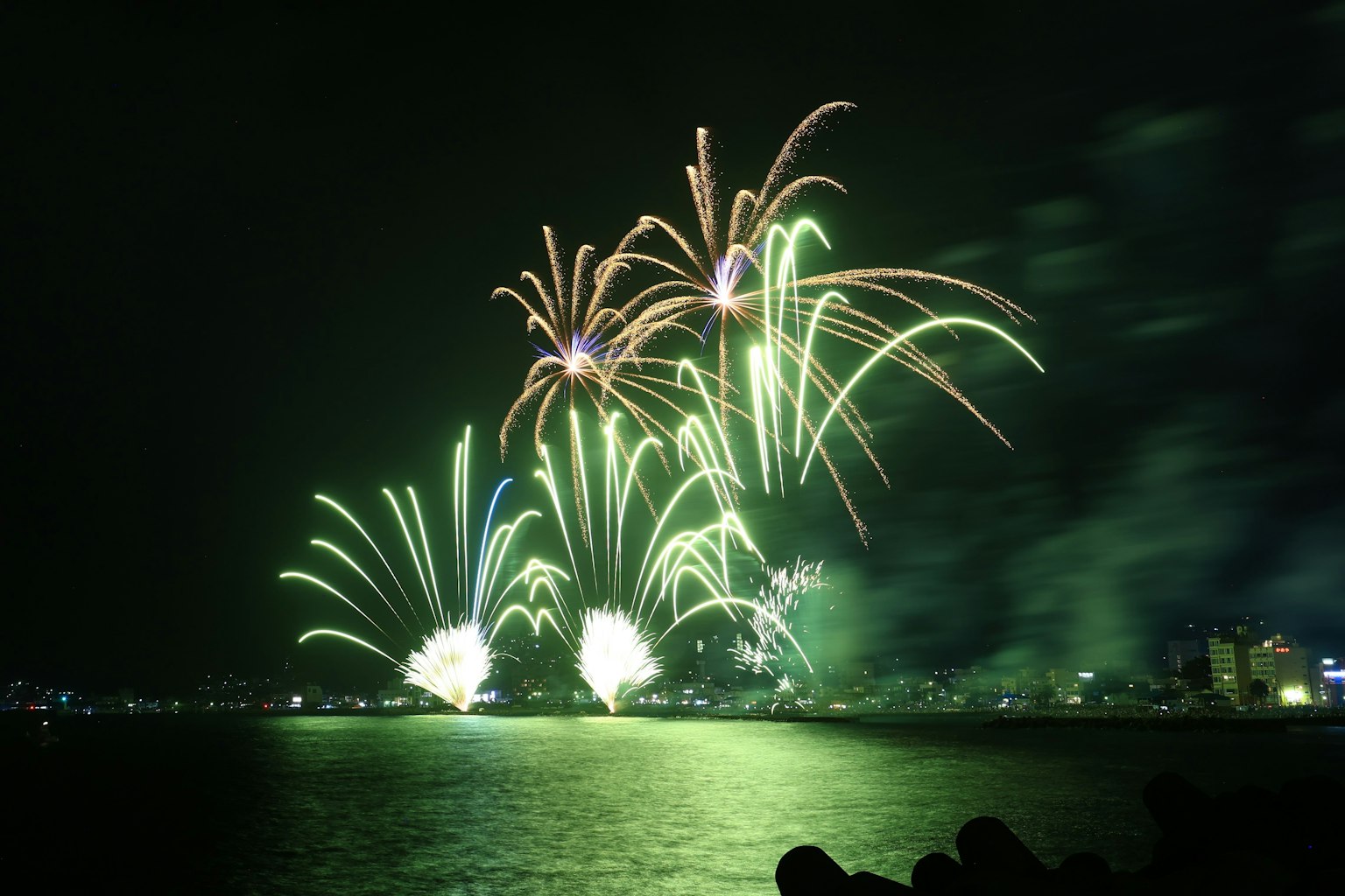 Bellissimo spettacolo di fuochi d'artificio verdi che si riflettono sull'acqua di notte