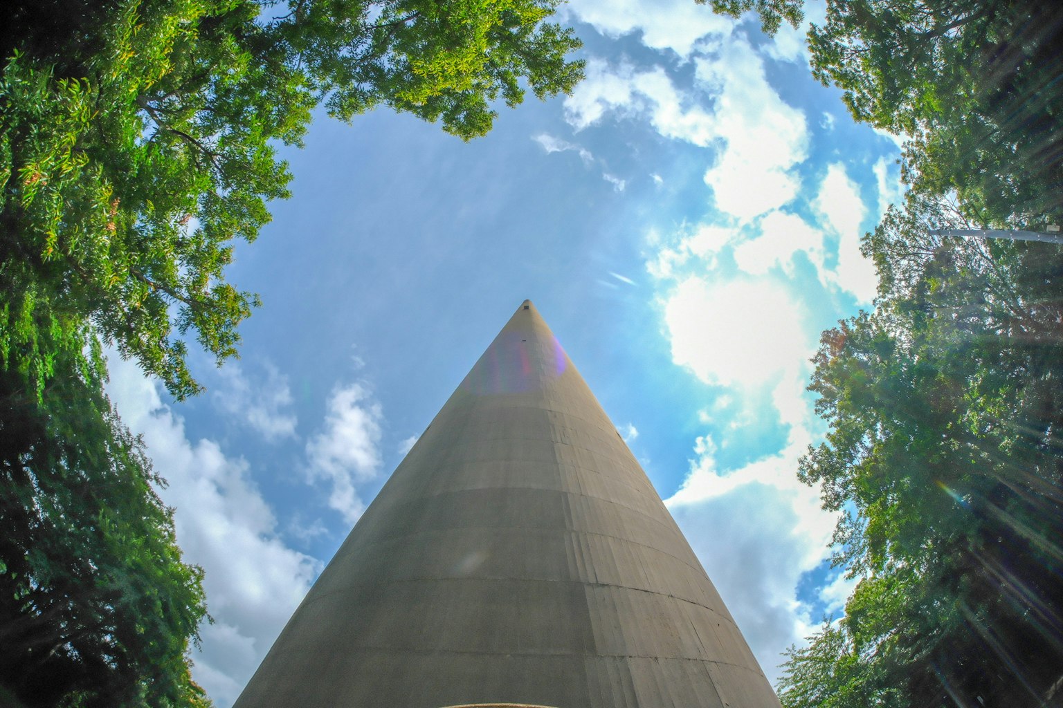 View looking up at a concrete spire surrounded by trees