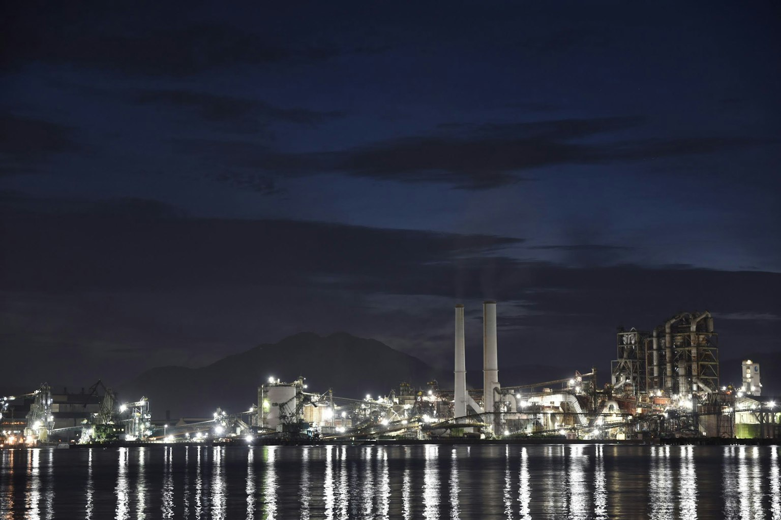 Night view of industrial area with factory chimneys and lights reflecting on water