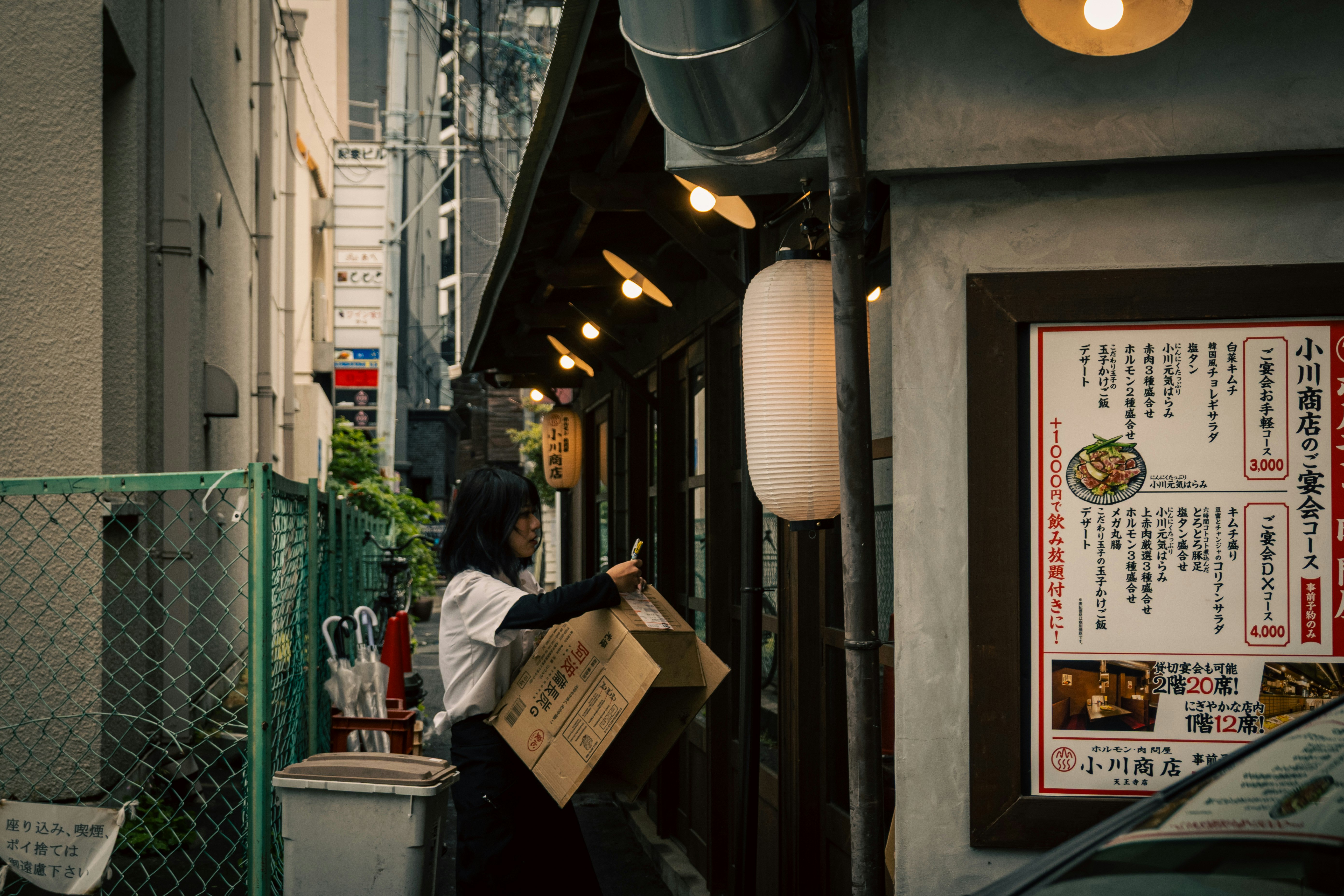 天王寺の路地で段ボールを持つ人と店先の看板が並ぶ商店街の軒先