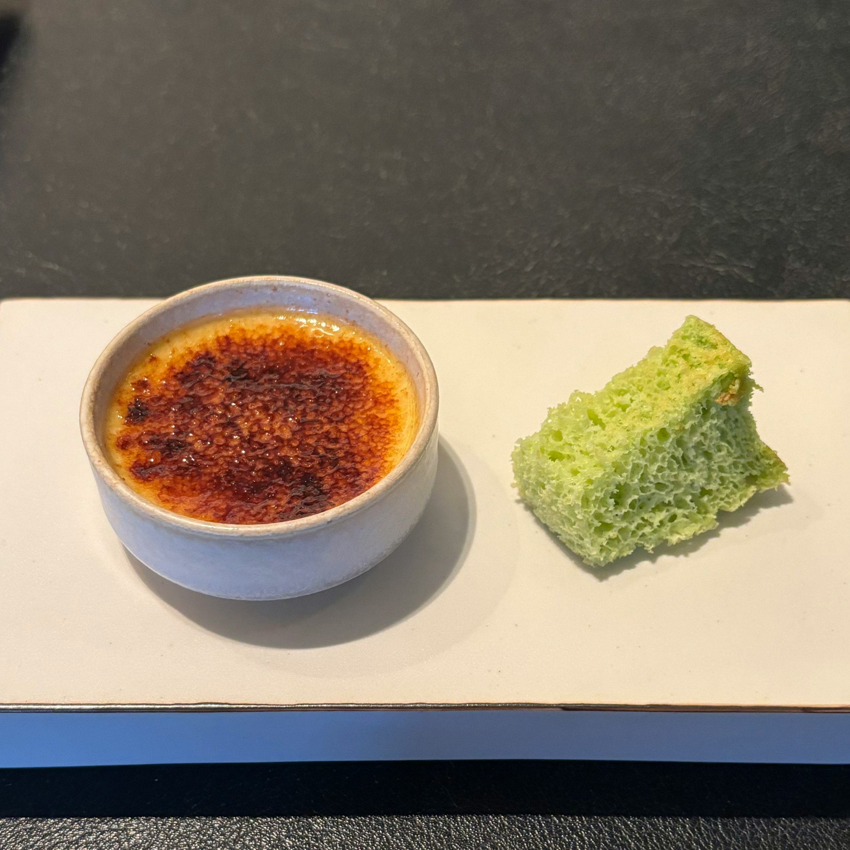 Crème brûlée in a blue ramekin with a green sponge dessert