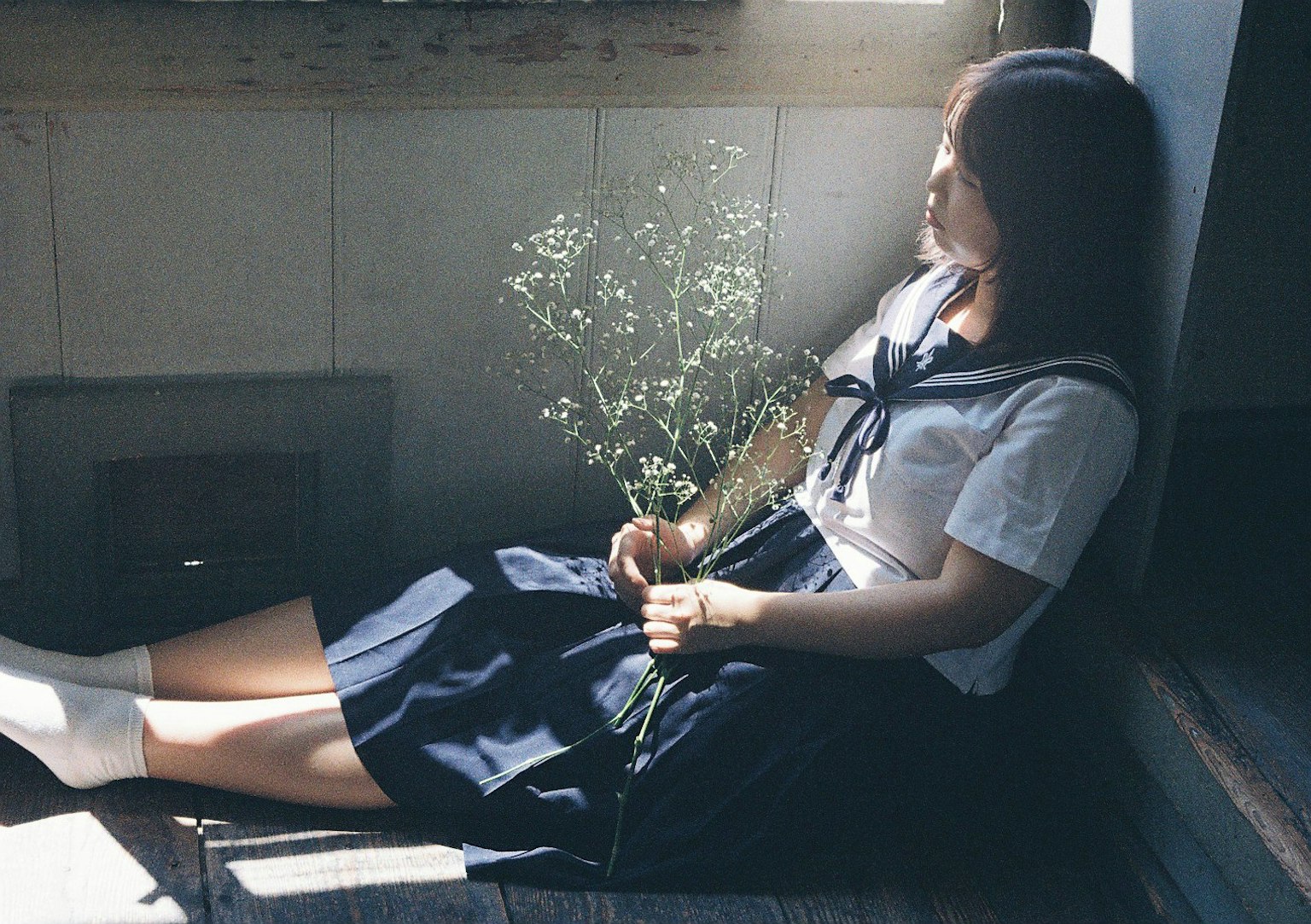 一个穿着校服的女孩静静地坐在窗边，手里拿着一束花