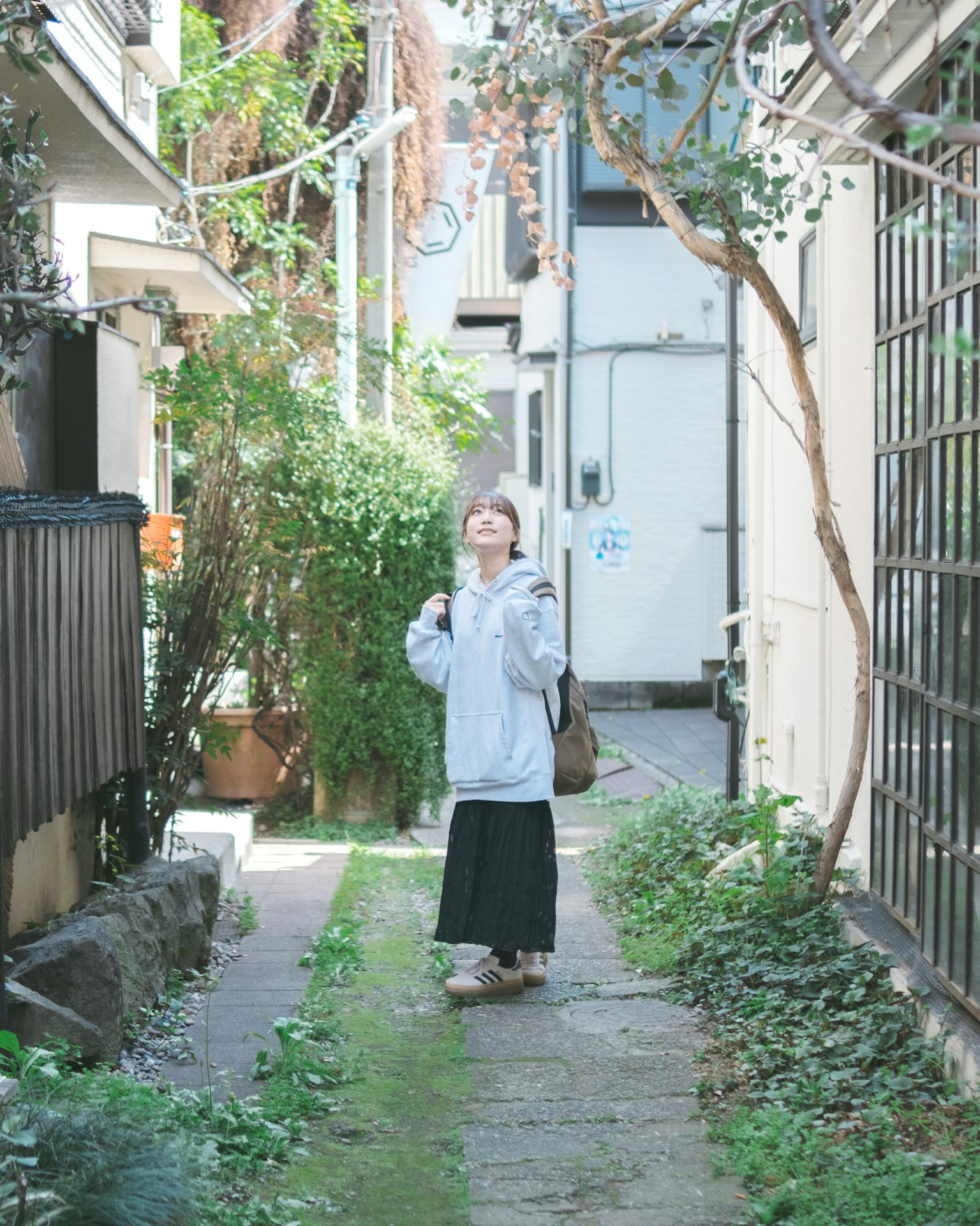 A smiling woman standing in a narrow alley surrounded by greenery