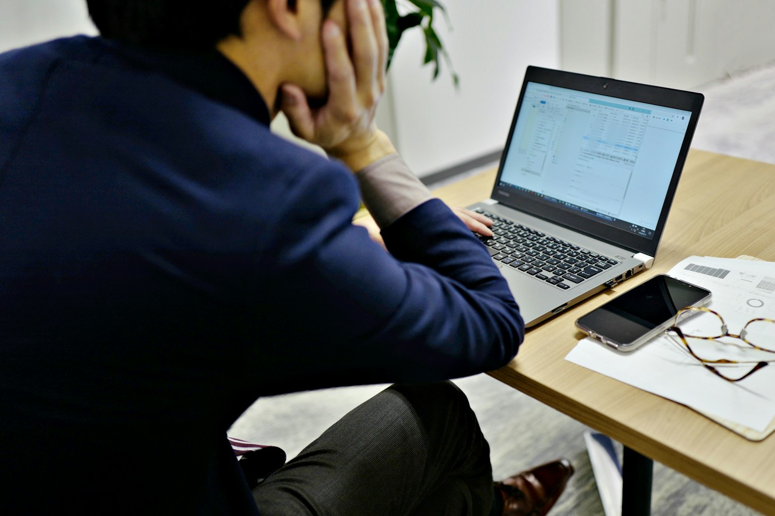 Un homme assis à un bureau regardant un ordinateur portable avec sa main sur son visage