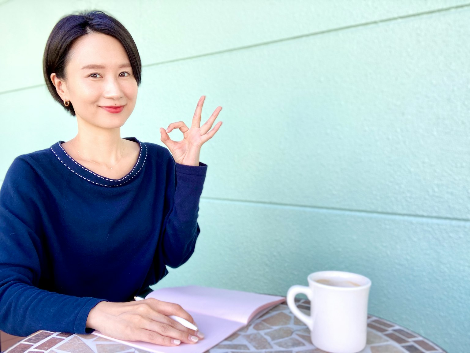Una donna in maglione blu che sorride e fa un segno OK con la mano