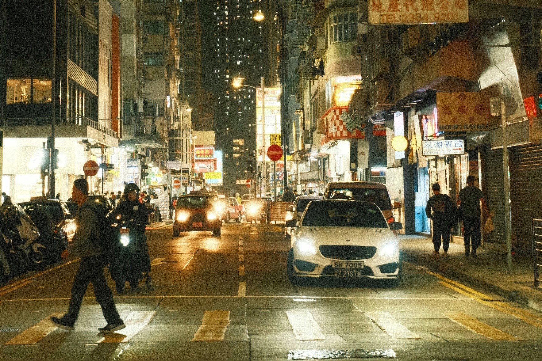 夜の香港の繁華街で車と歩行者が交差するシーン