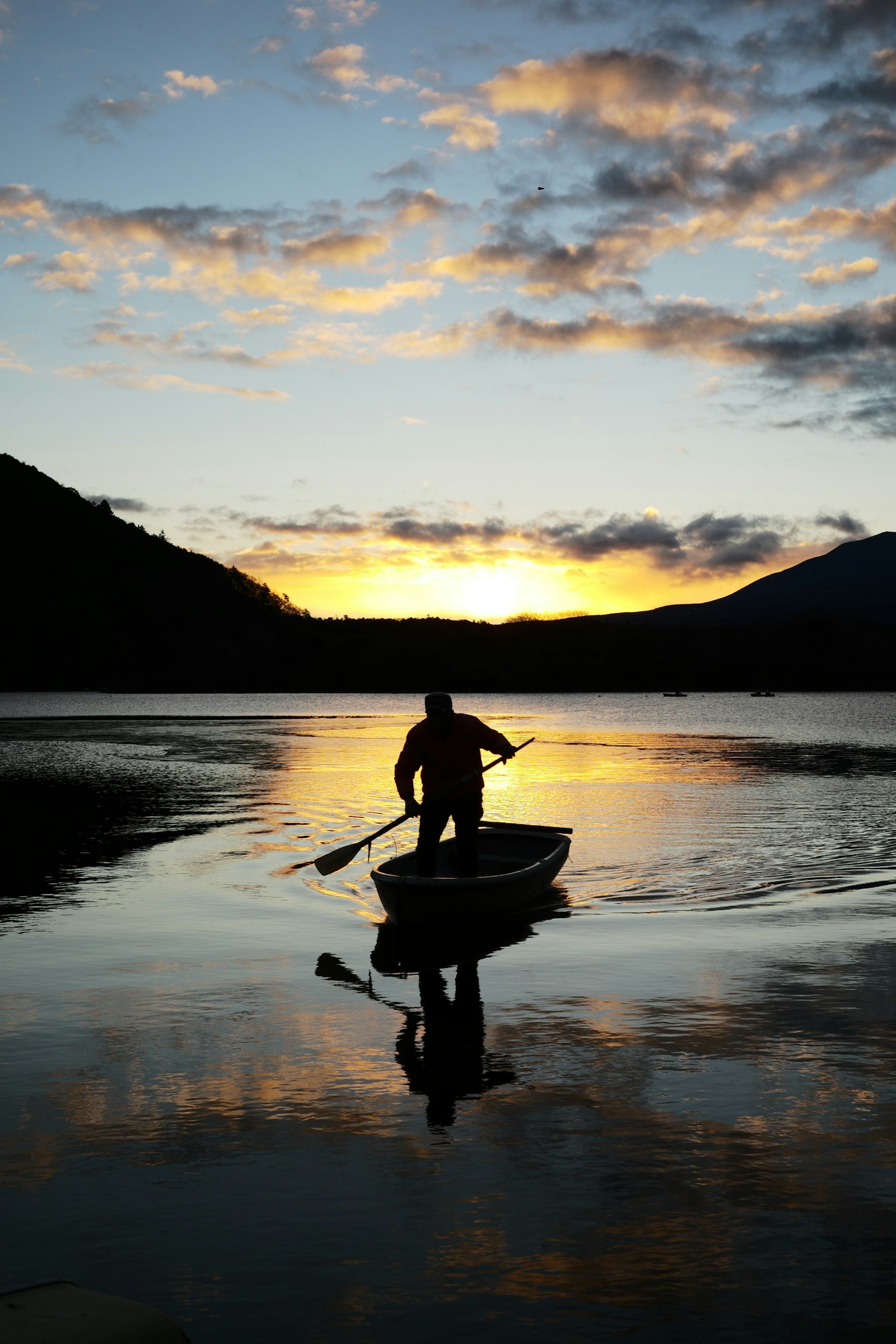Silhouette of a man rowing a boat on a calm lake beautiful sunset reflection