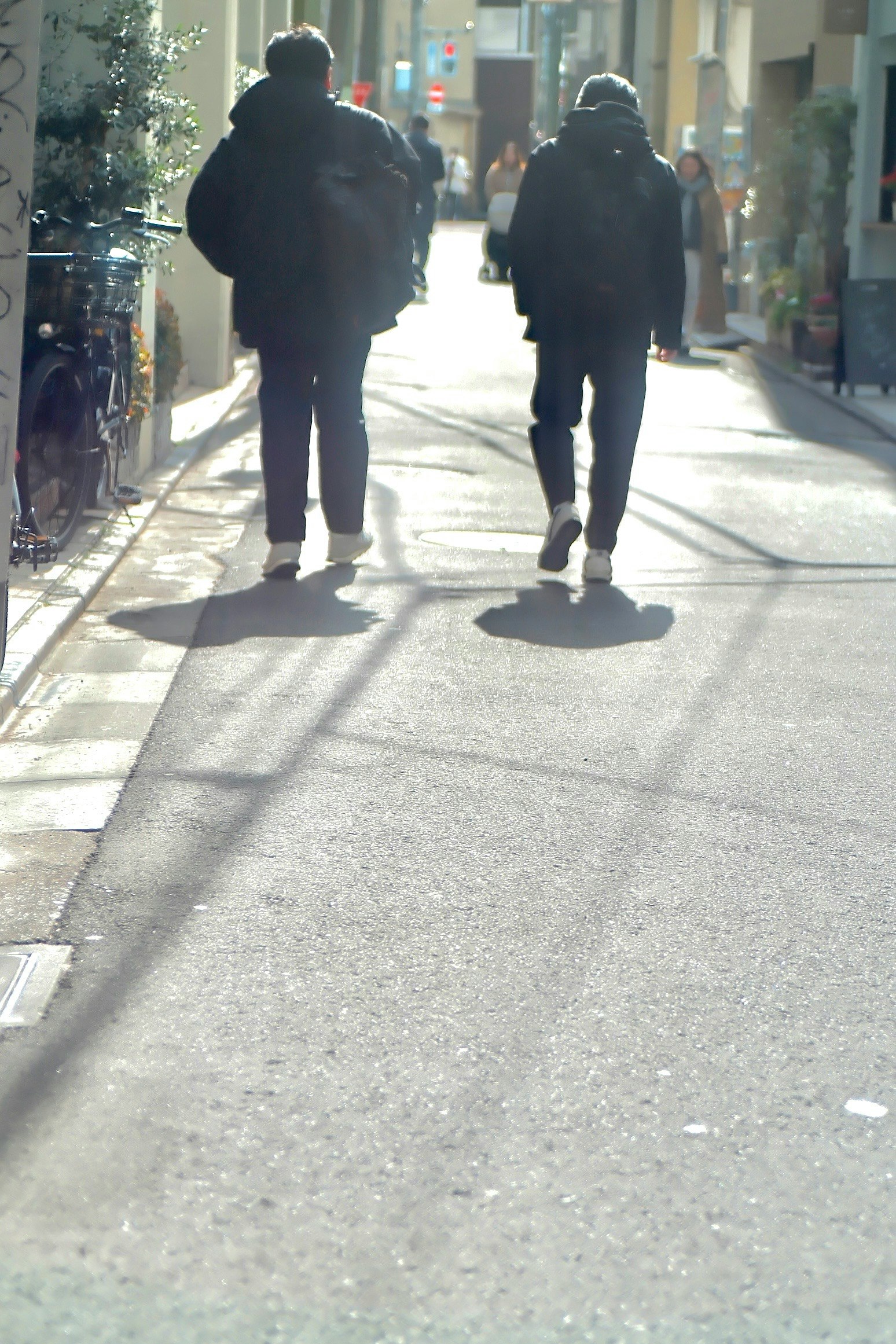 路地を歩く人々の後ろ姿が見える街の通り
