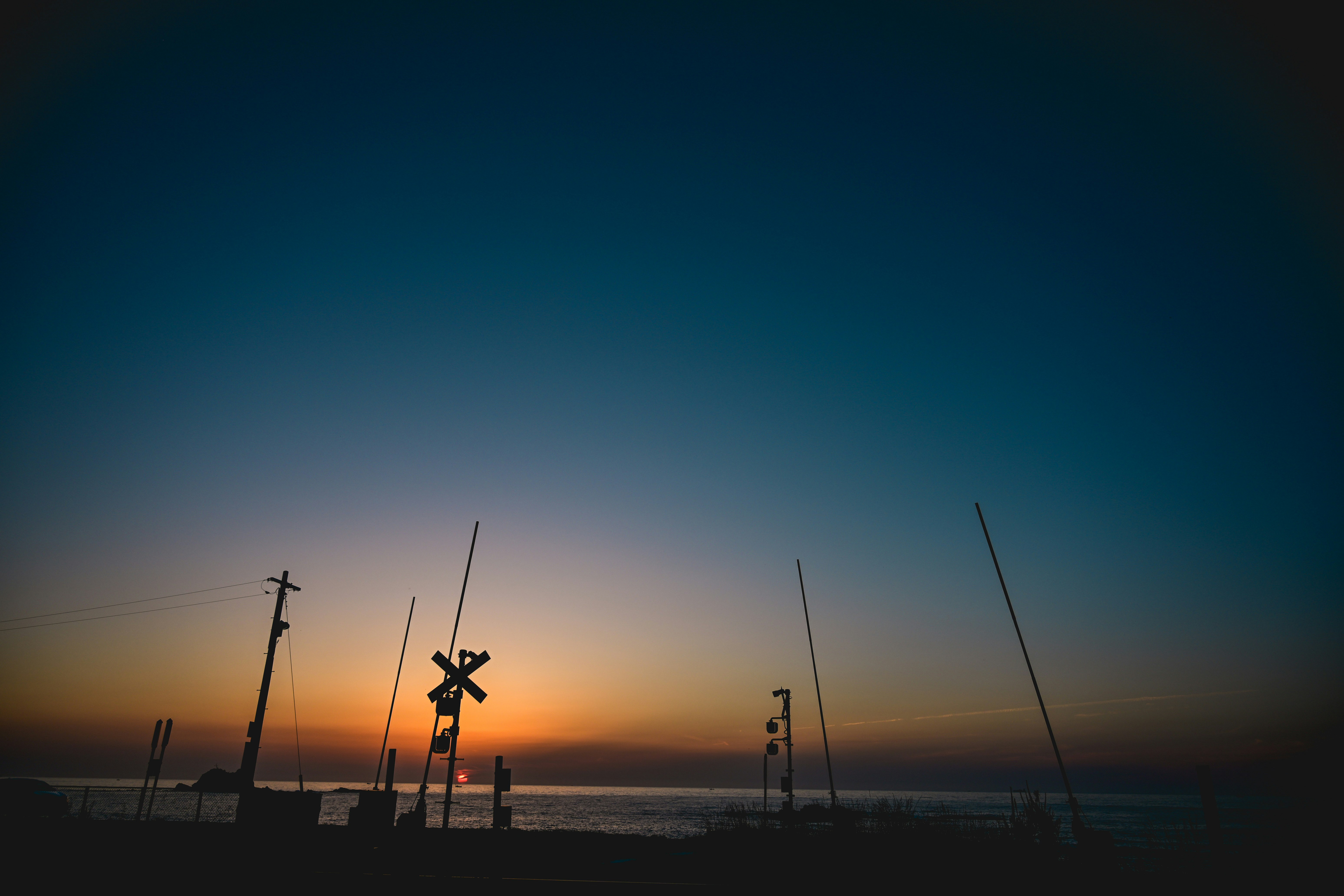 silhouettes of wind turbines and power poles on a seaside at sunset