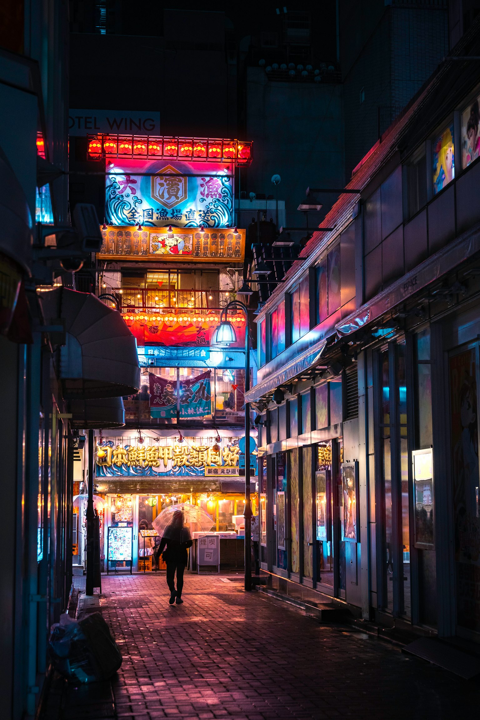 Une rue étroite illuminée par des néons la nuit avec une personne marchant