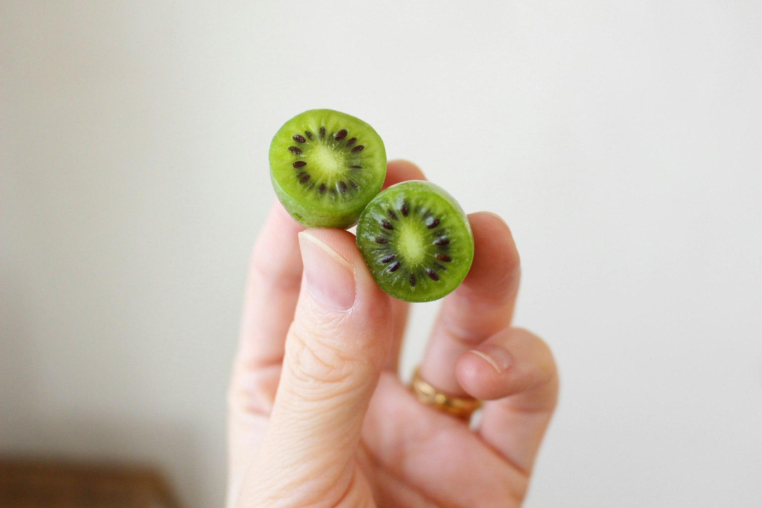 Hand holding two sliced kiwis showing green flesh and black seeds