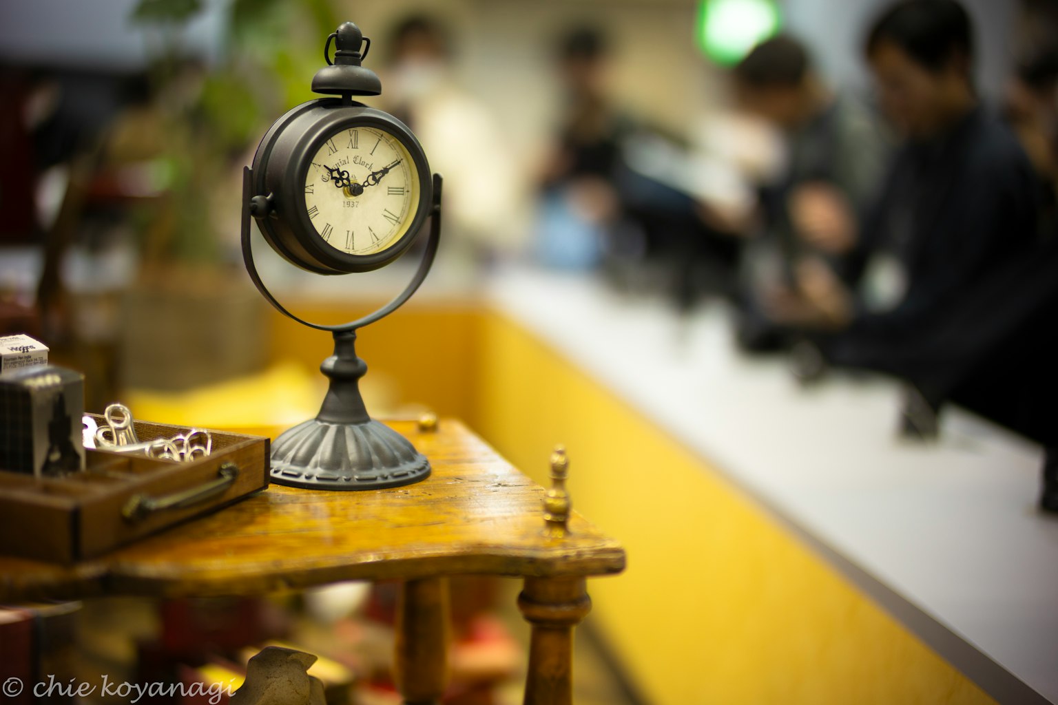 Horloge antique sur une table en bois avec des personnes floues en arrière-plan