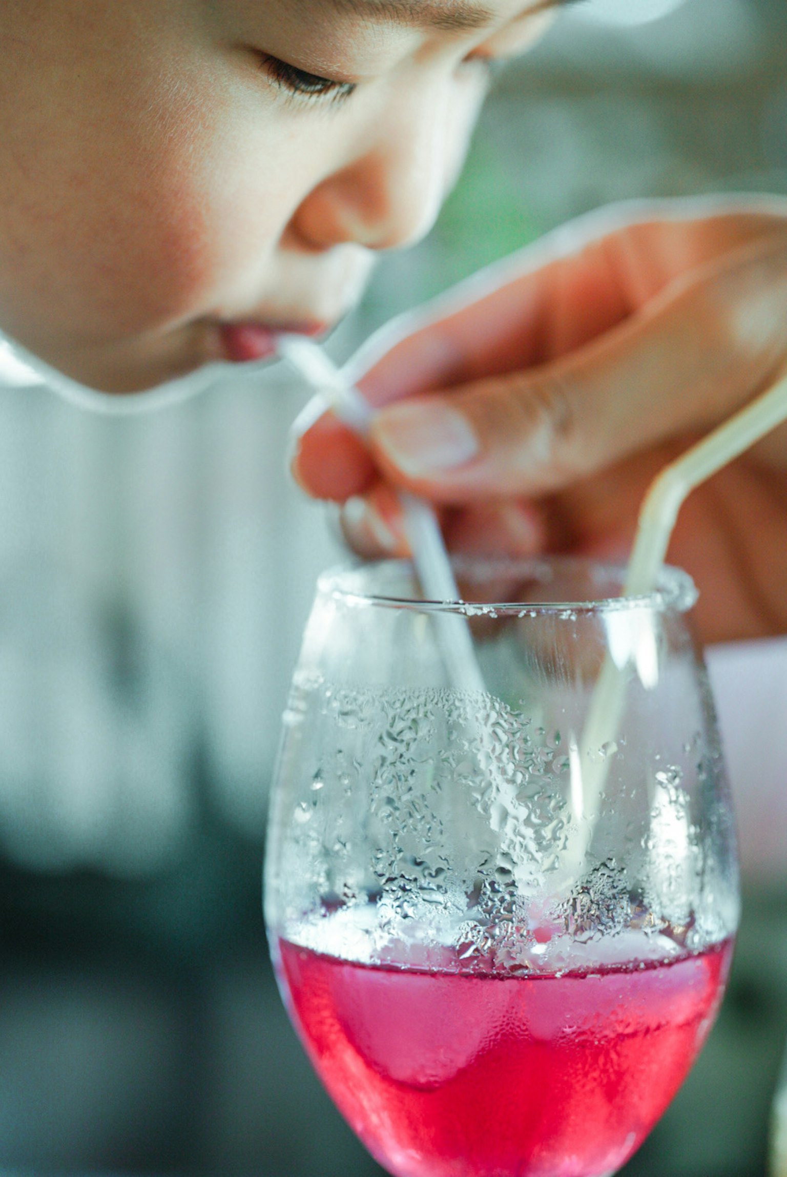 Anak sedang minum dari gelas dengan sedotan Tangan dewasa membantu dengan sedotan Gelas berisi minuman merah muda