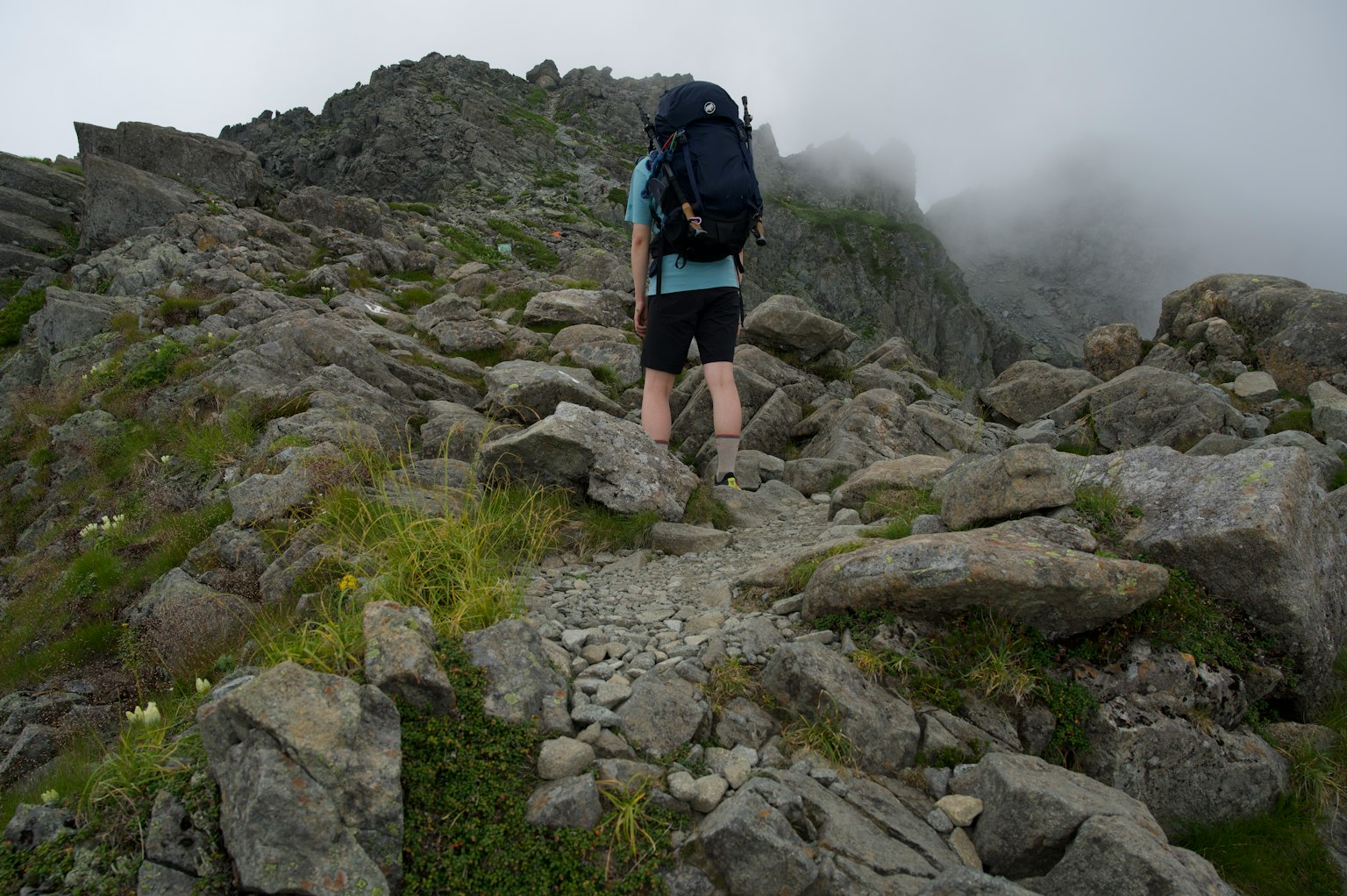 Wanderer, der einen felsigen Bergpfad in Nebel hinaufsteigt