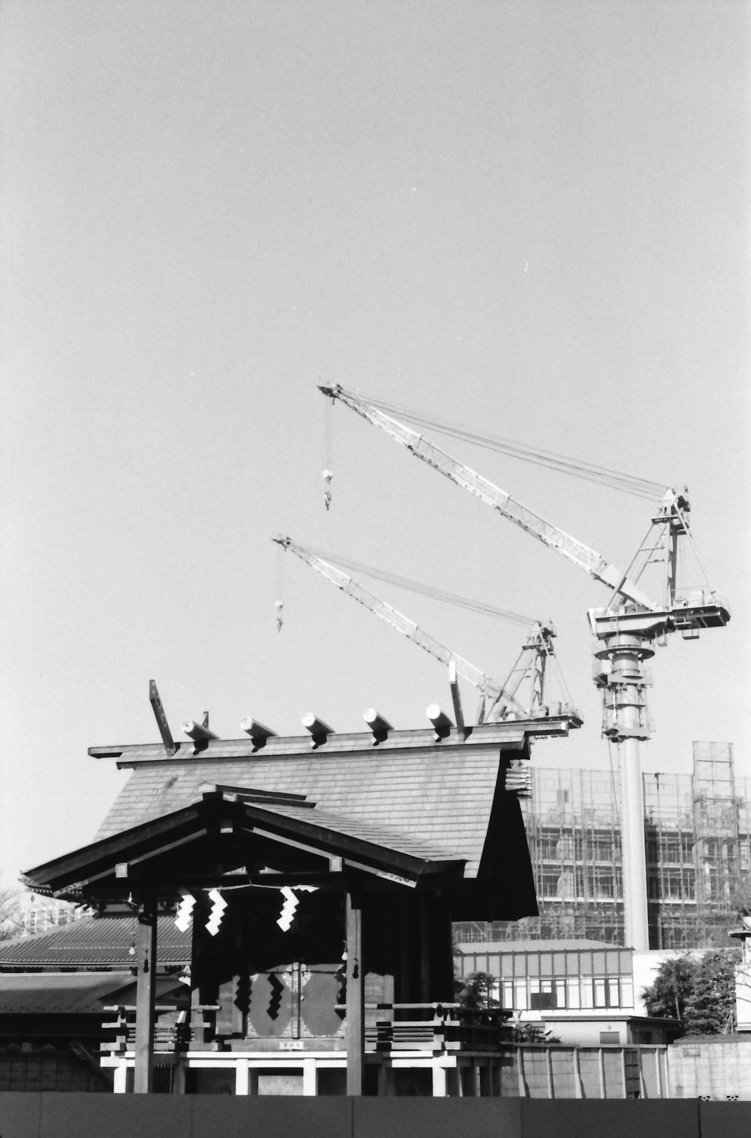 Foto en blanco y negro que presenta el techo de un santuario tradicional y grúas de construcción